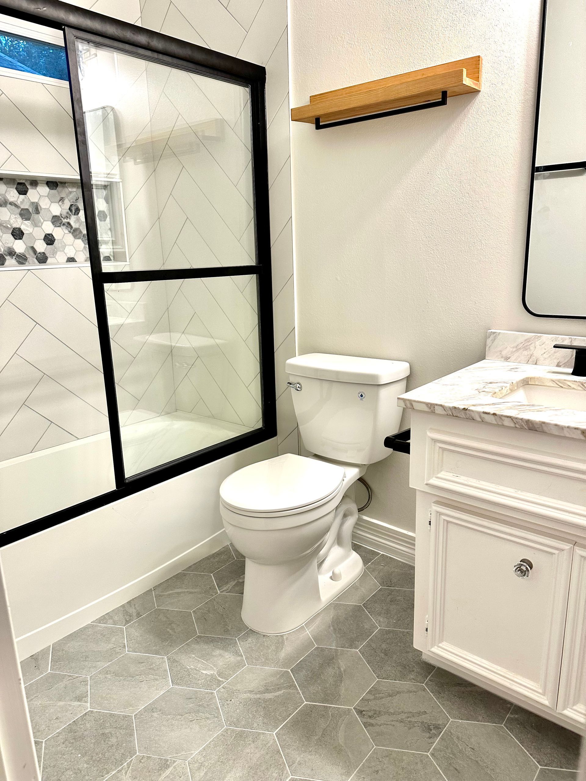 Bright bathroom with walk-in shower, toilet, vanity cabinet, and wood towel shelf.