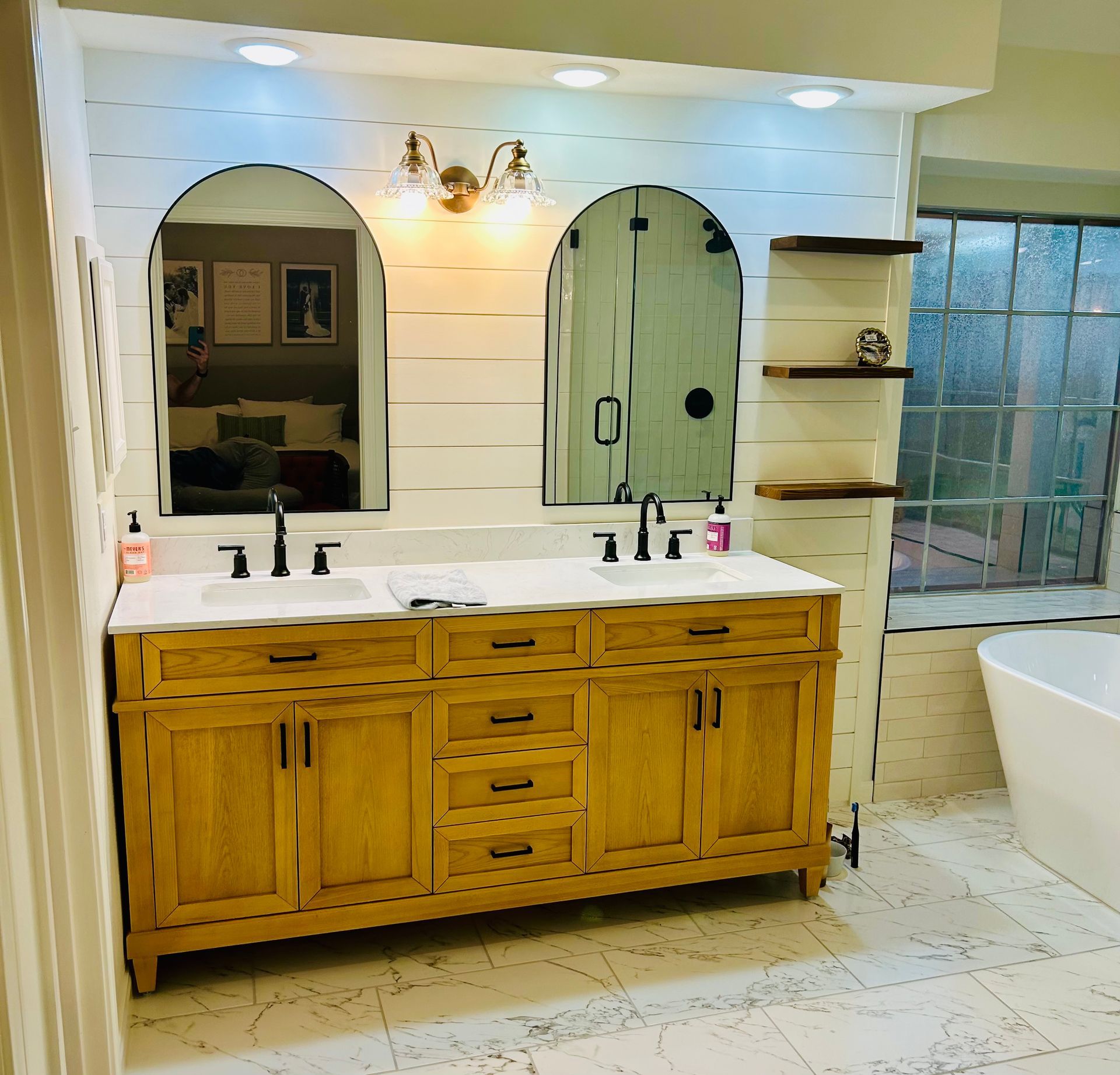 Double vanity bathroom with arched mirrors, white shiplap walls, and honey-colored wood cabinets