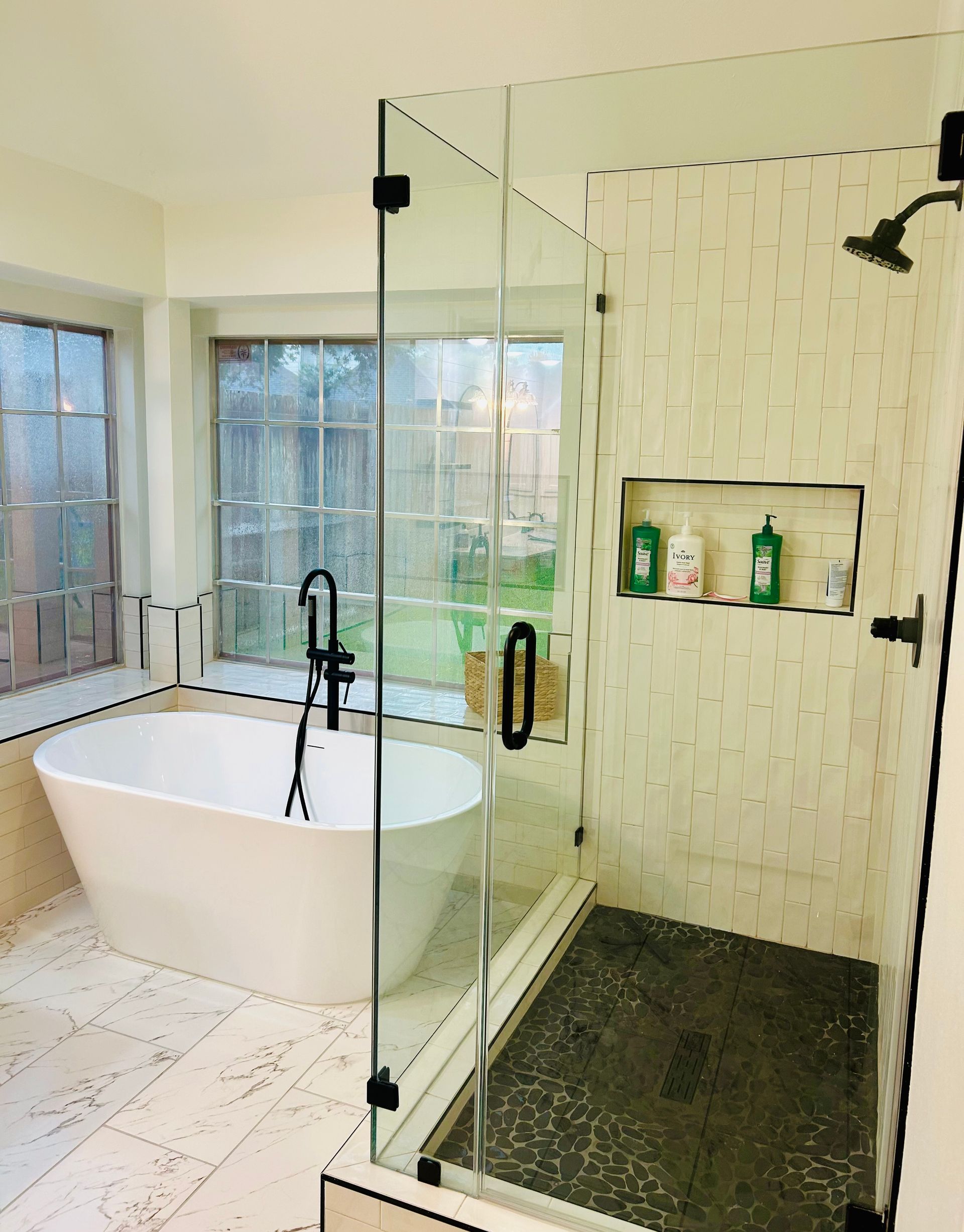 Modern bathroom with freestanding tub, glass shower, and wall niche of toiletries