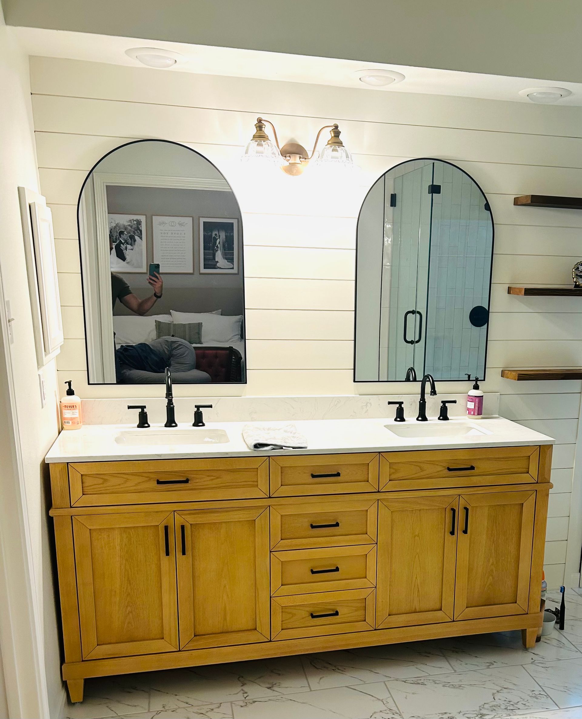 Wooden bathroom vanity with double sinks, arched mirrors, and wall sconces in a bright modern bathroom