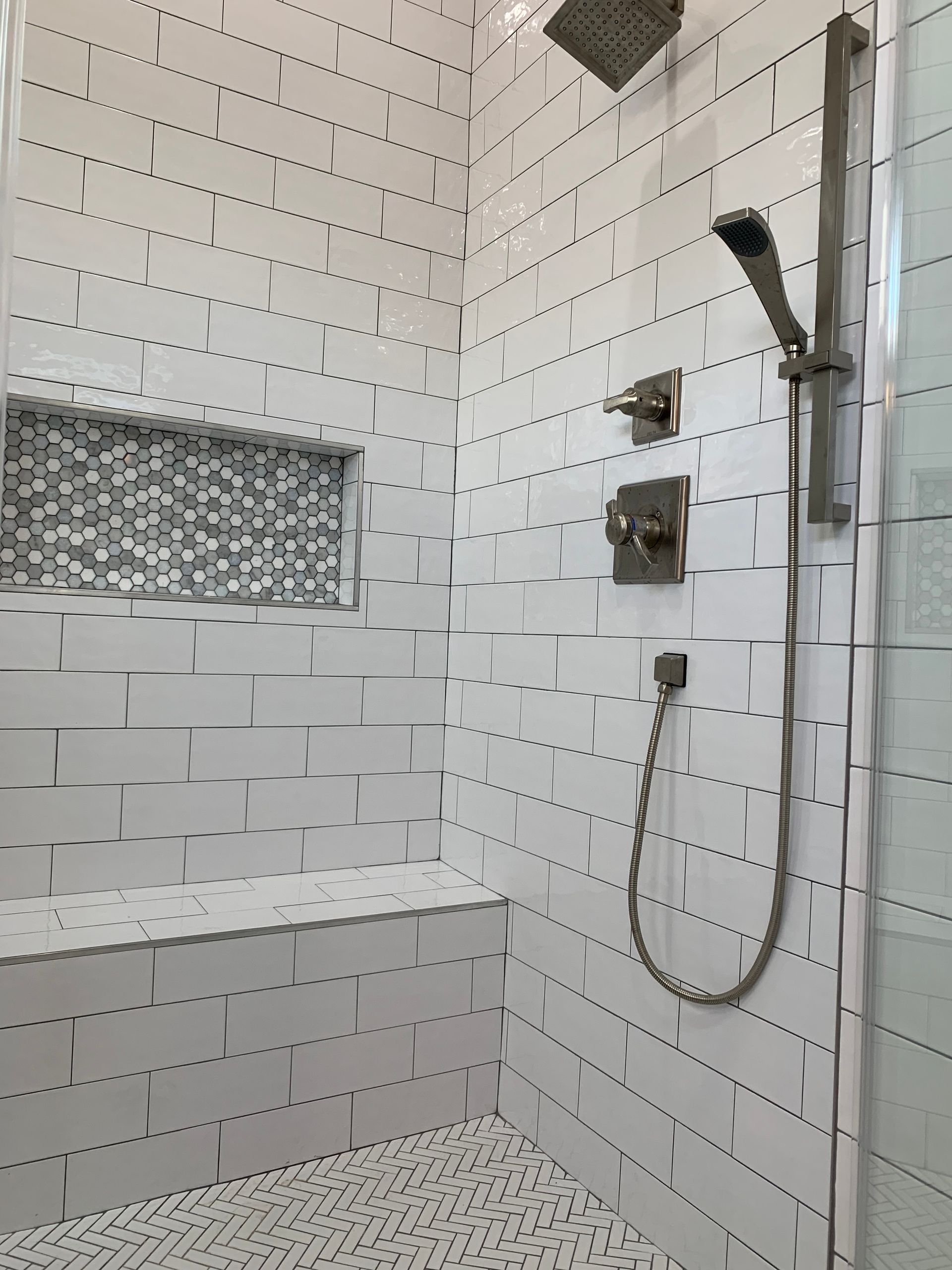 Modern tiled shower with mosaic accent niche, wall-mounted shower controls, and handheld showerhead