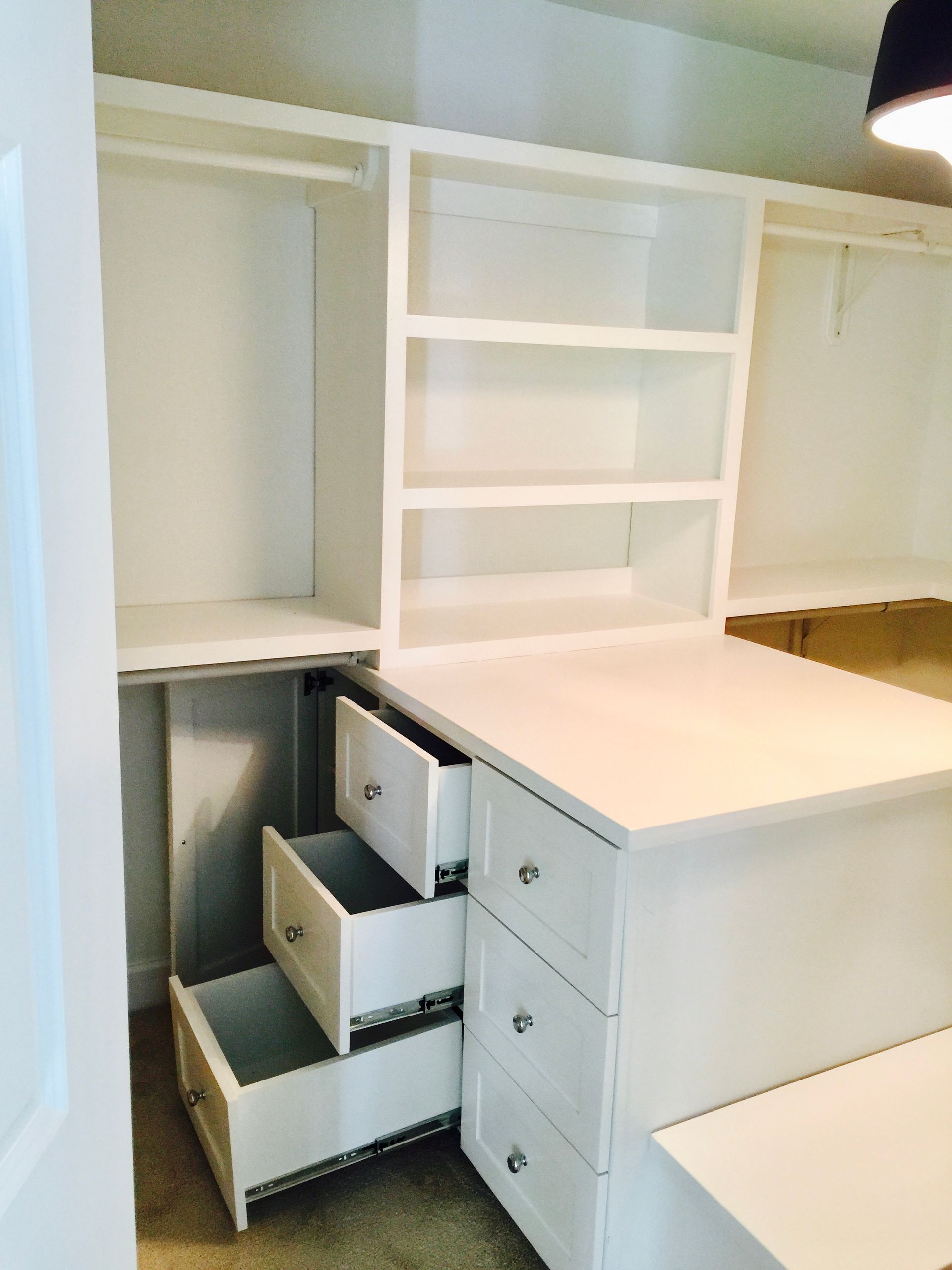 White built-in desk and shelving with open drawers in a closet or office nook