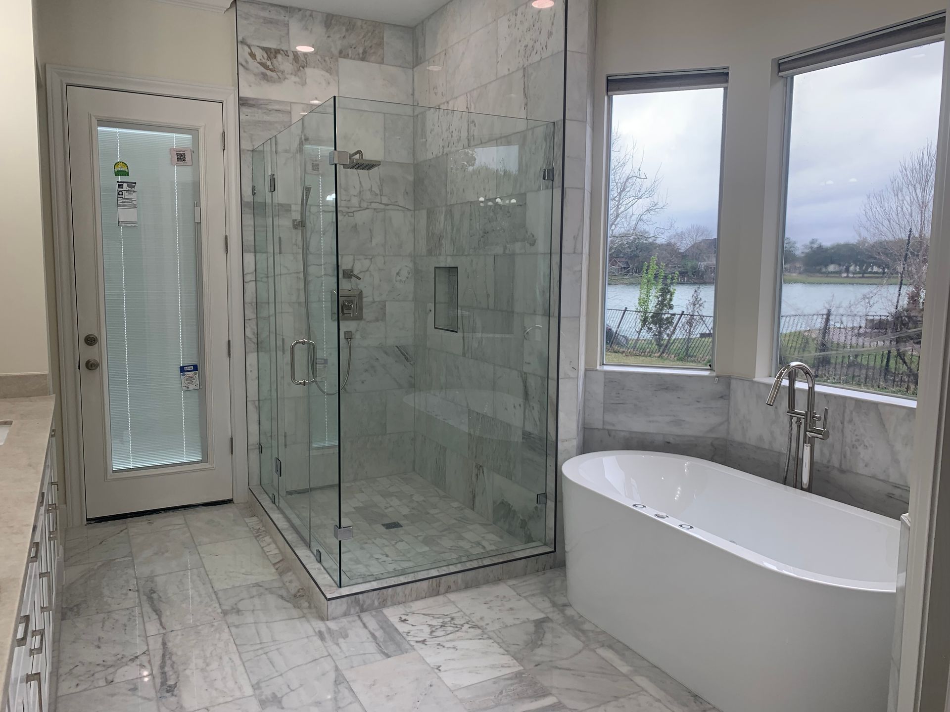 Modern bathroom with glass shower, freestanding tub, and large windows overlooking water