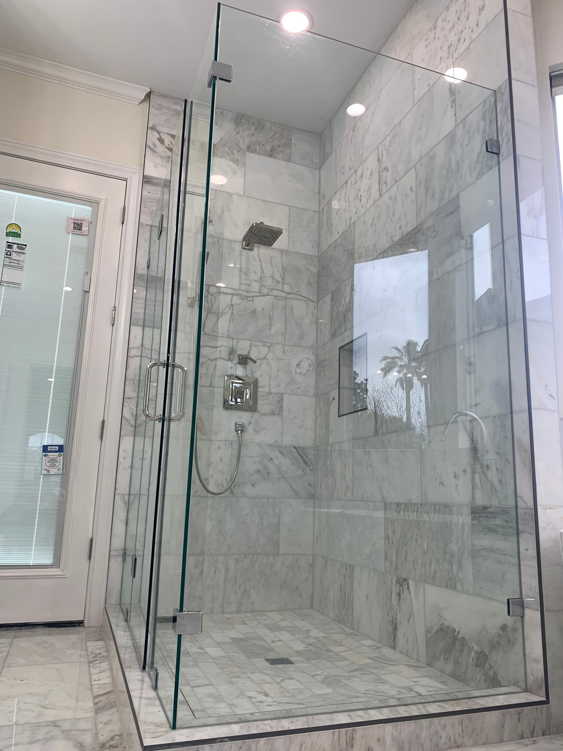 Glass walk-in shower with marble-look tile and chrome fixtures in a bright bathroom