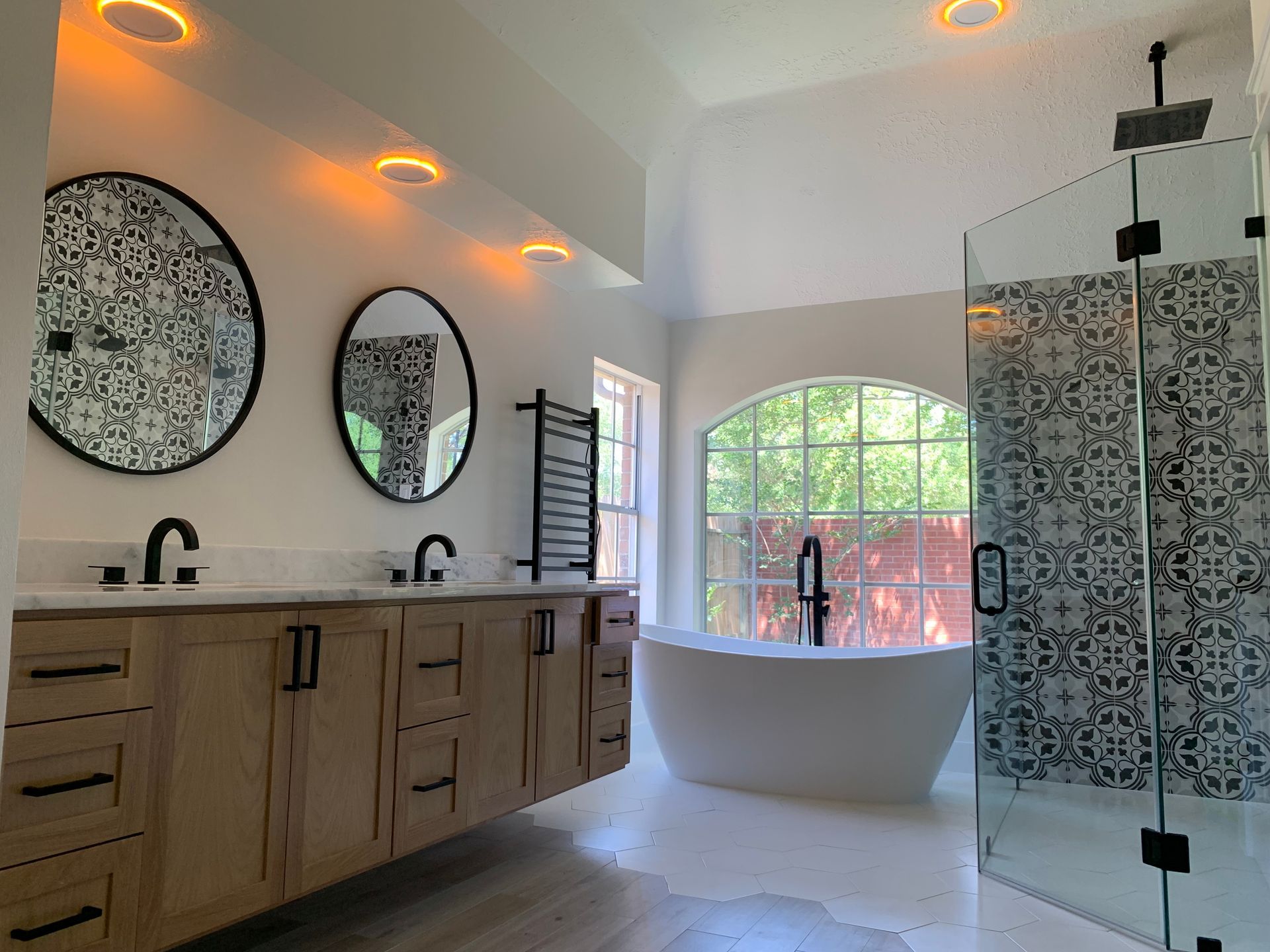 Modern bathroom with double vanity, round mirrors, and freestanding tub by a large window.