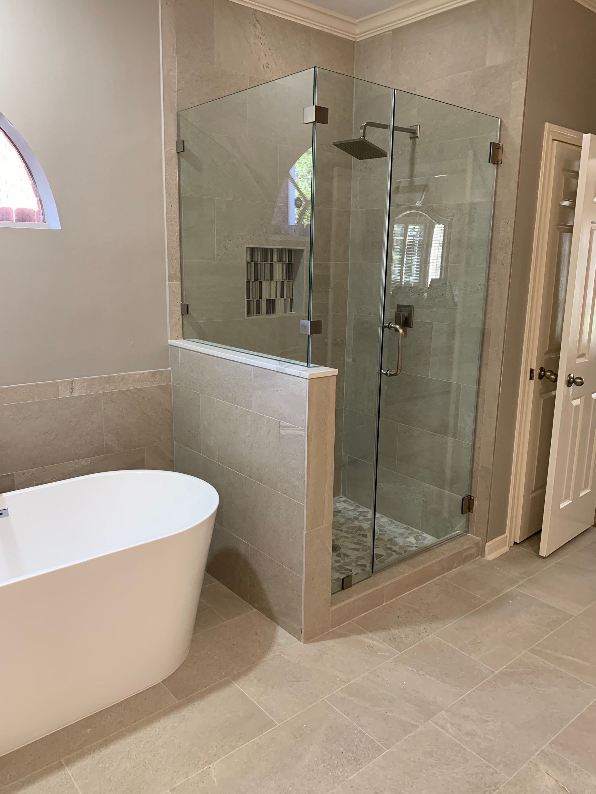 Modern bathroom with a glass-enclosed shower, freestanding tub, and beige tile floor.