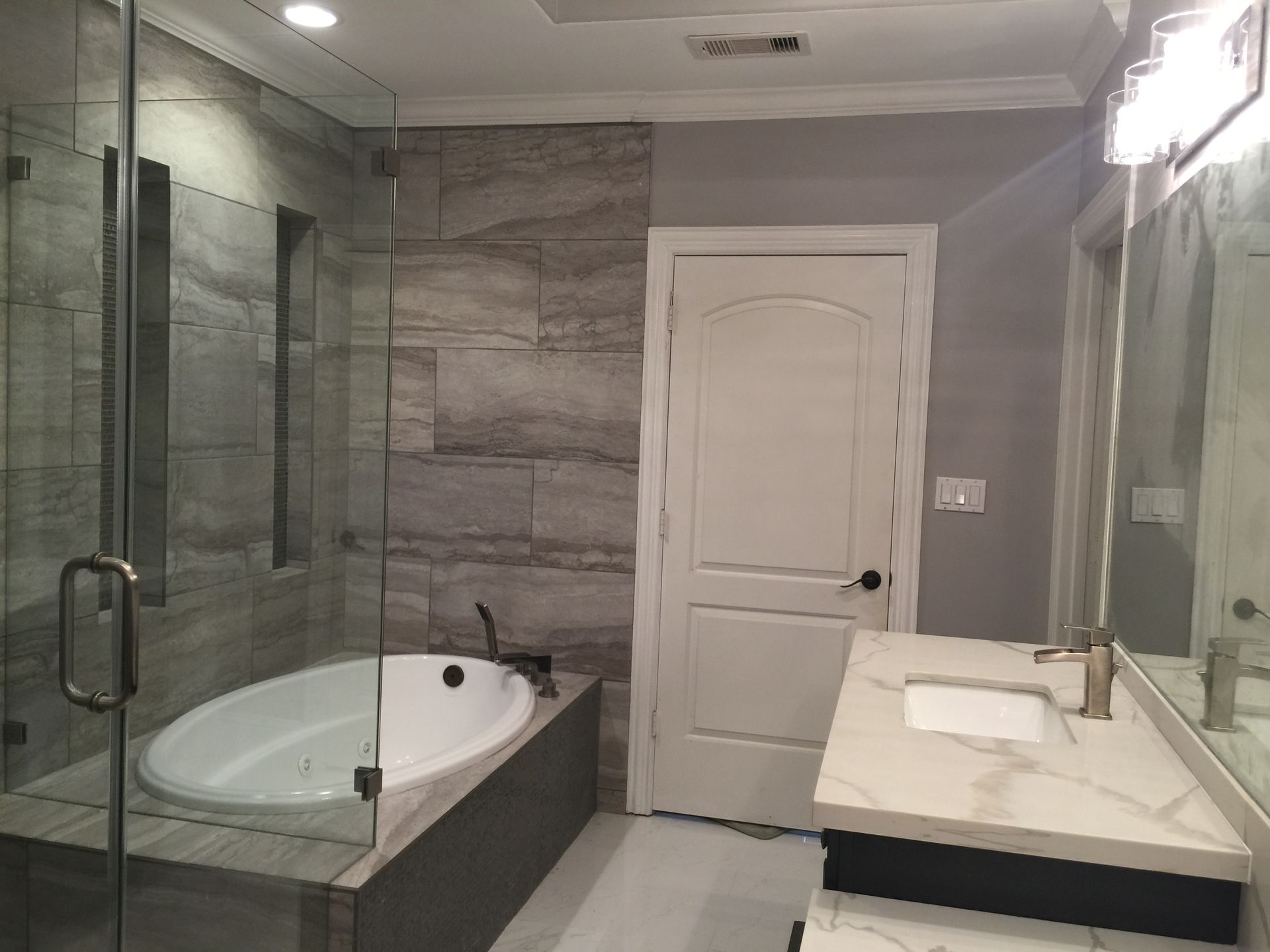 Modern bathroom with glass shower, corner tub, vanity sink, and white door