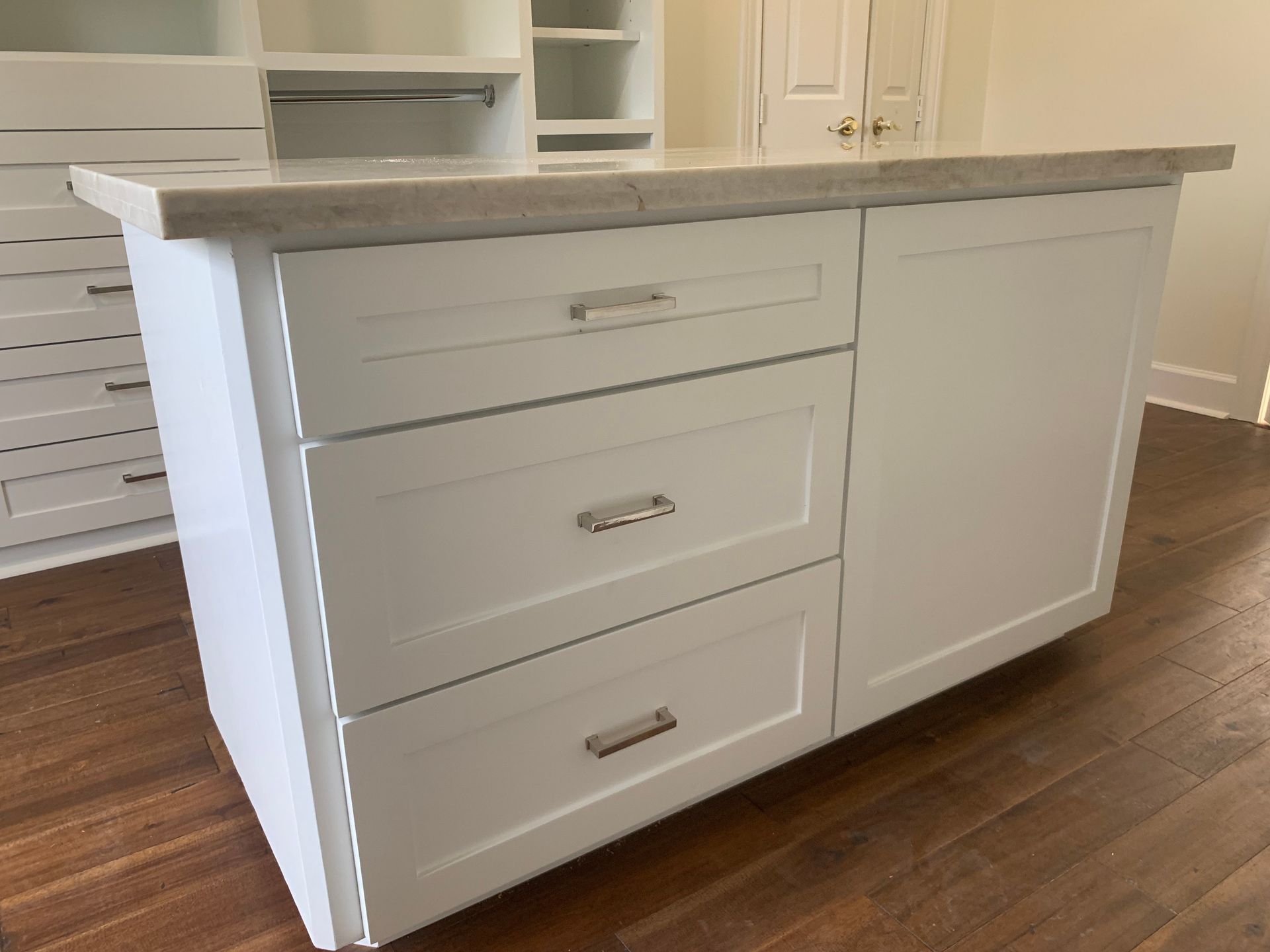 White kitchen island with gray countertop and three drawers in a bright room
