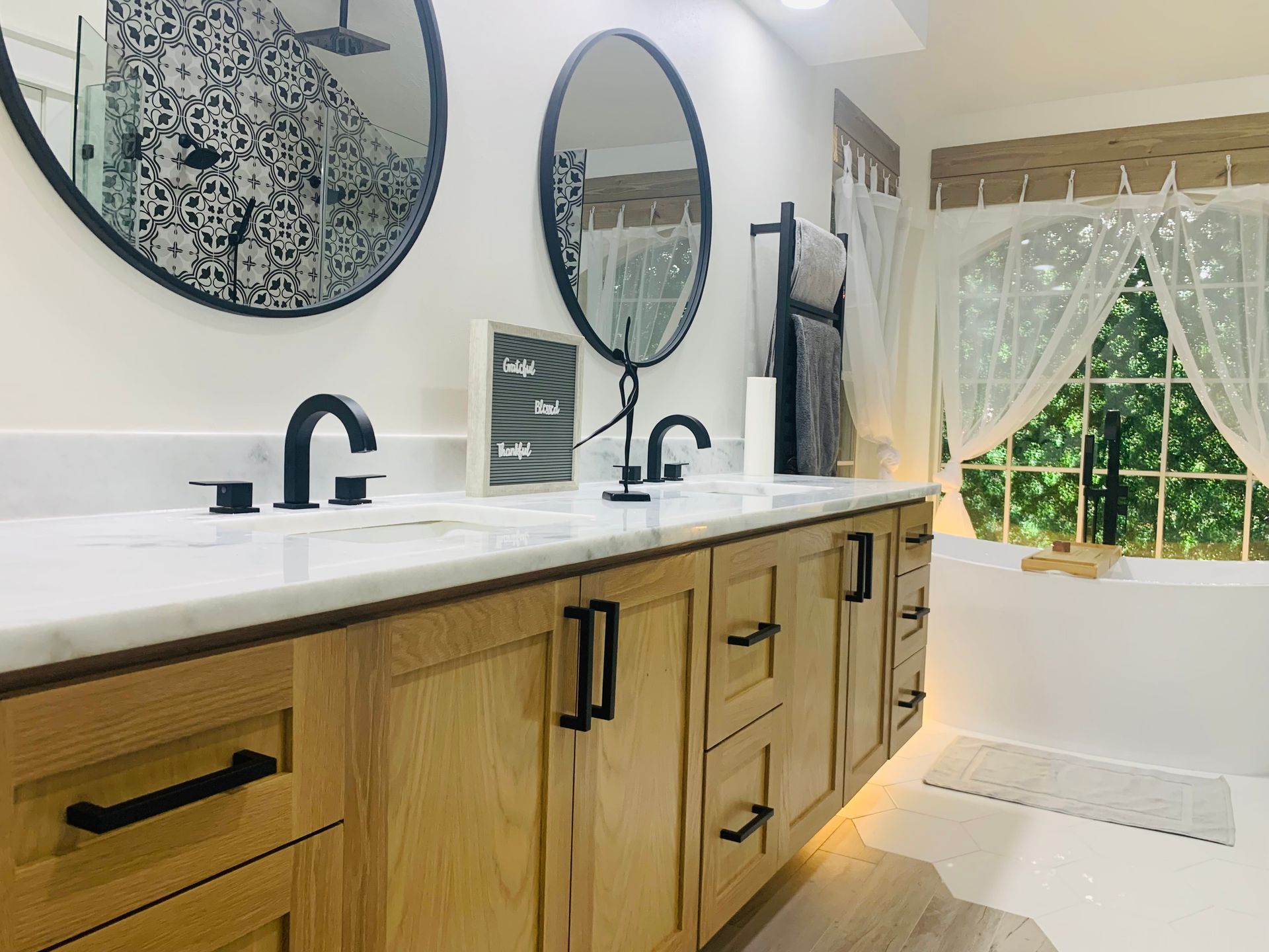 Modern bathroom vanity with double sinks, round mirrors, and a bright window with sheer curtains