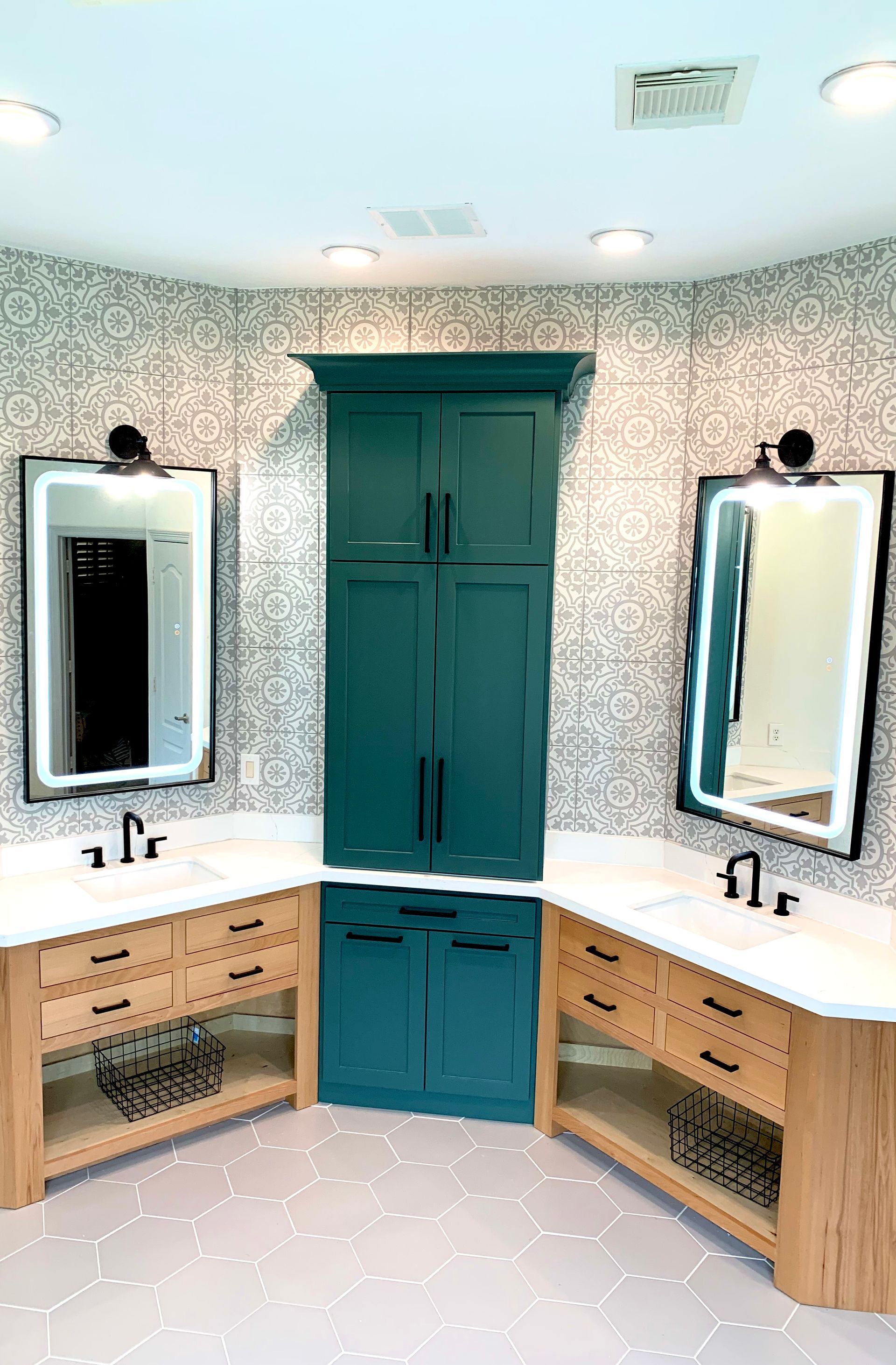 A small bathroom vanity area with two mirrors, white countertops, wood cabinets, and teal cabinet doors.