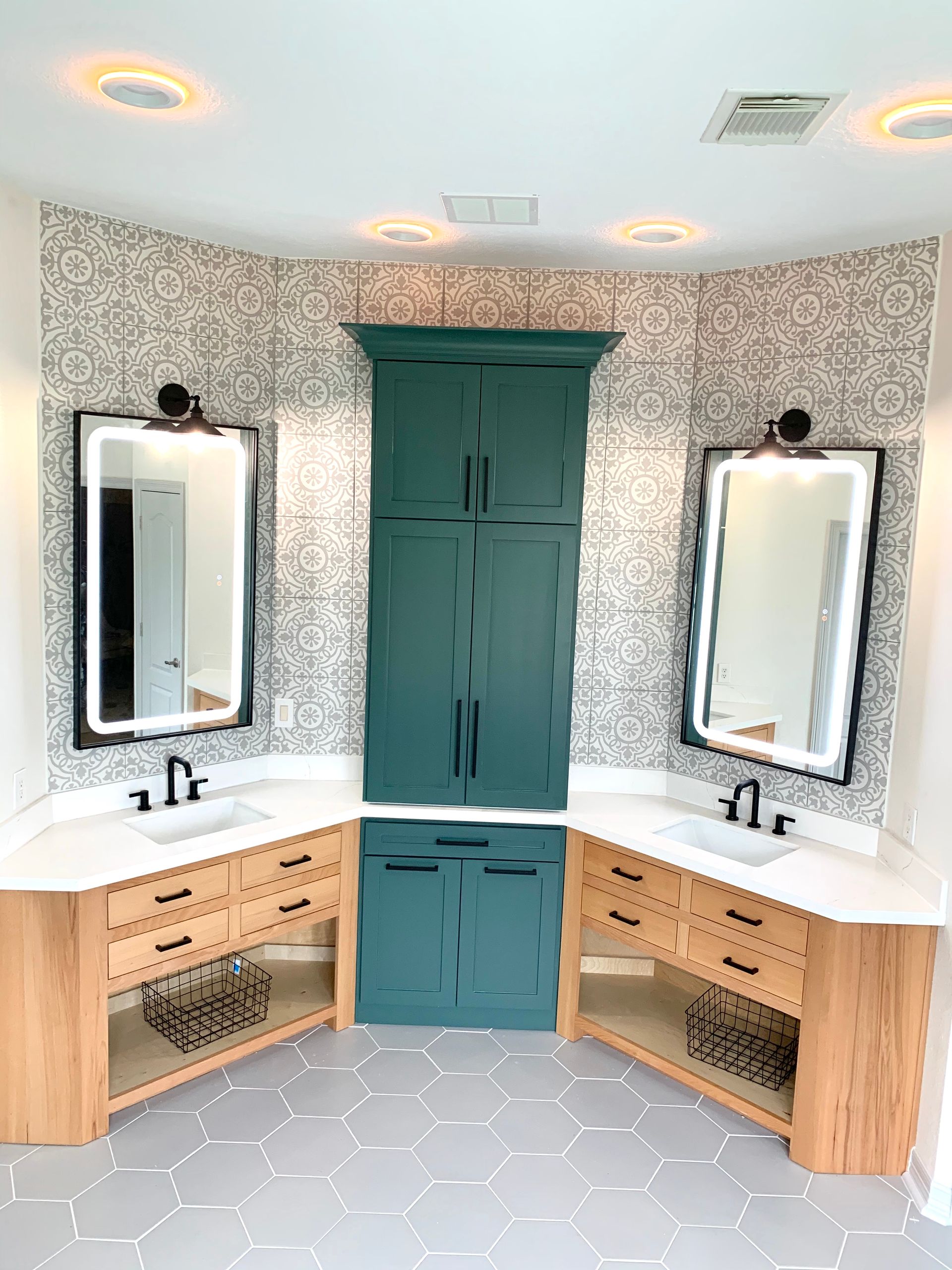 Bright bathroom vanity with two mirrors, teal cabinets, floral wallpaper, and hexagon tile floor.