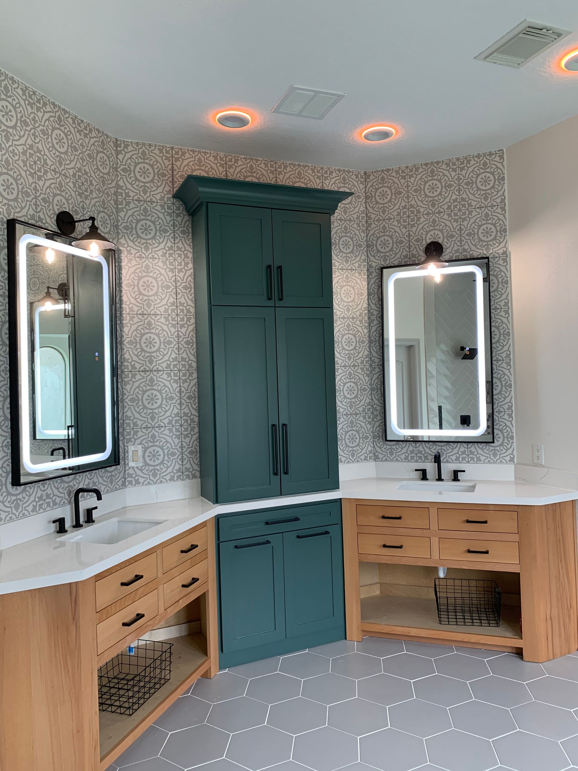 Modern bathroom with twin mirrors, wood vanities, teal cabinets, and patterned wallpaper.