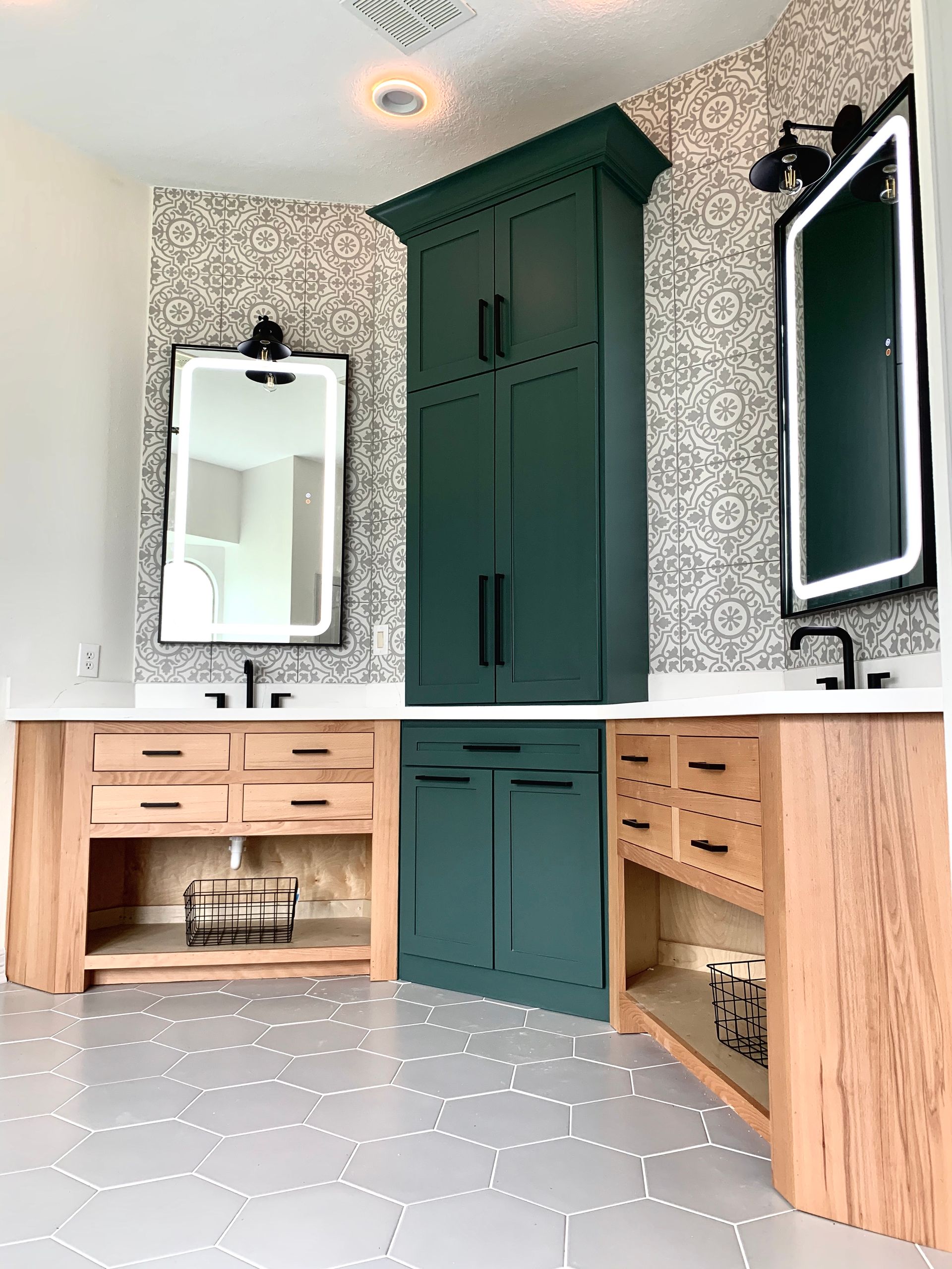 Modern bathroom vanity with dark green cabinets, wood drawers, white sink, and patterned floor and wallpaper