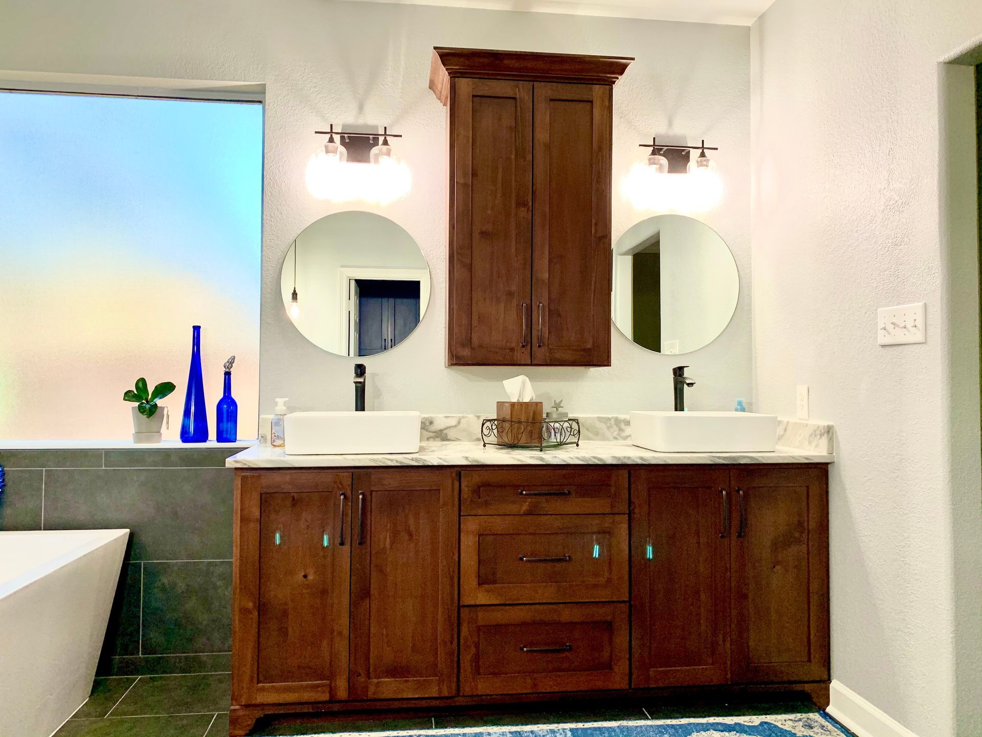 Modern bathroom vanity with double sinks, round mirrors, wood cabinets, and blue bottles on the counter