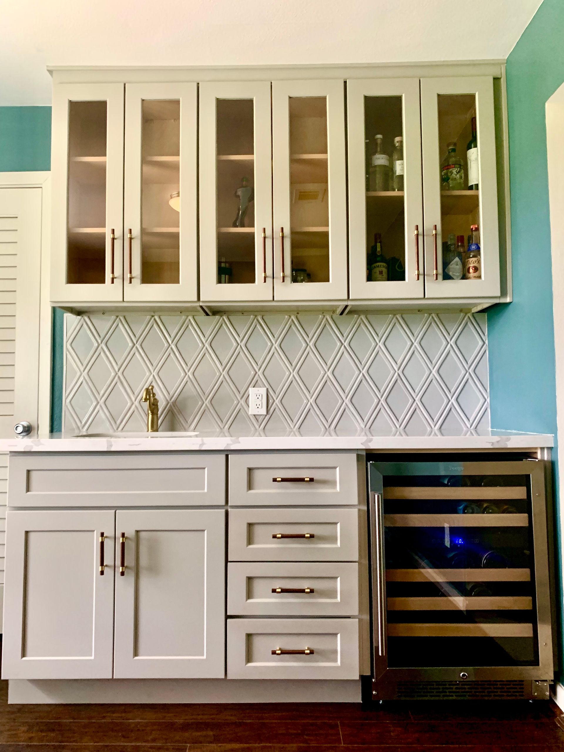Modern kitchen with white cabinets, glass-front uppers, marble tile backsplash, and stainless wine cooler.