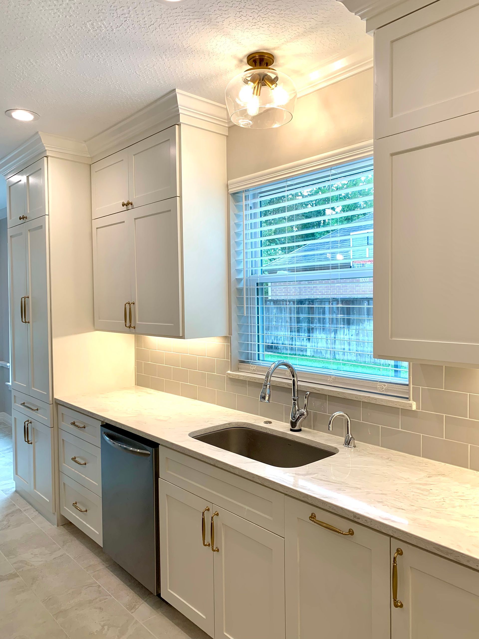 Bright white kitchen with long countertop, sink under window, and stainless dishwasher and cabinets