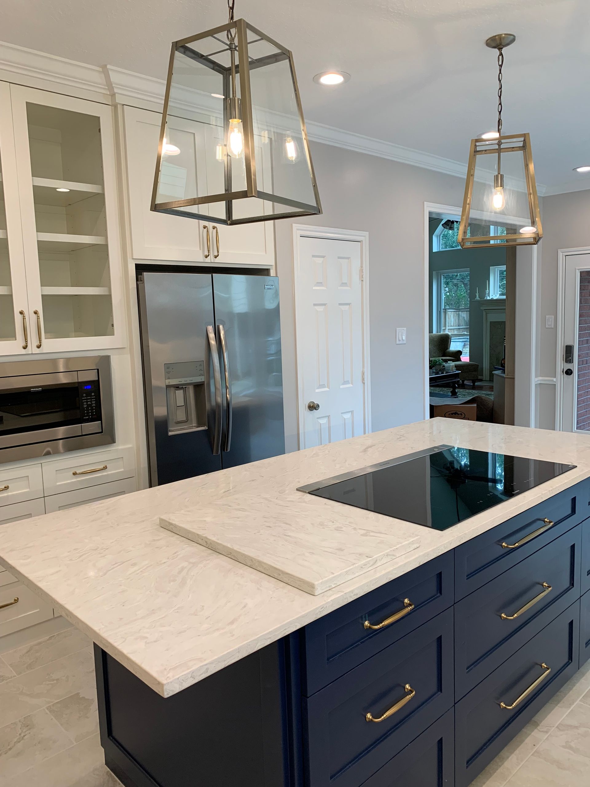 Modern kitchen island with white marble countertop, navy cabinets, pendant lights, and stainless steel fridge.