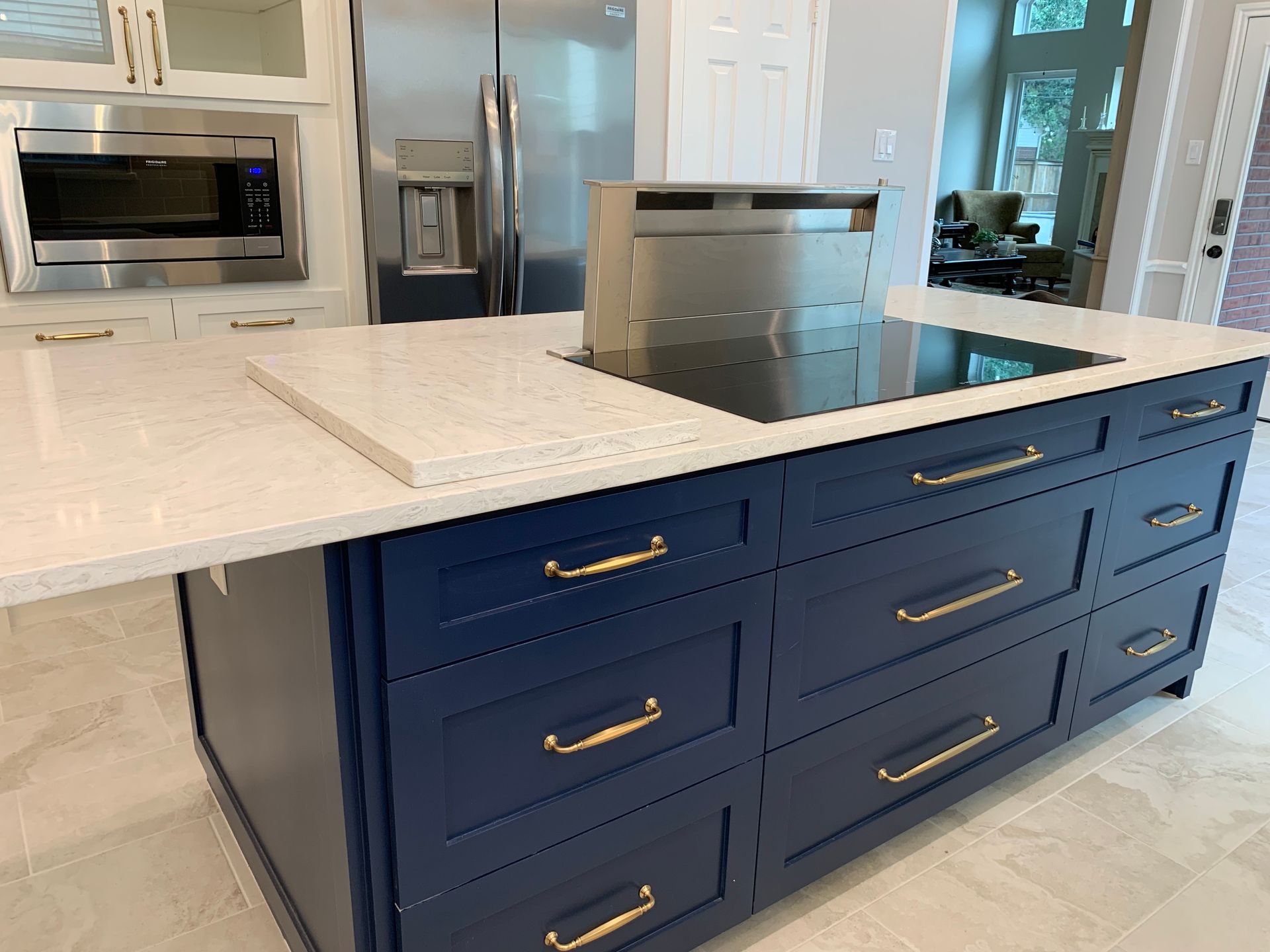 Kitchen island with navy drawers and brass handles beneath a white countertop and cooktop