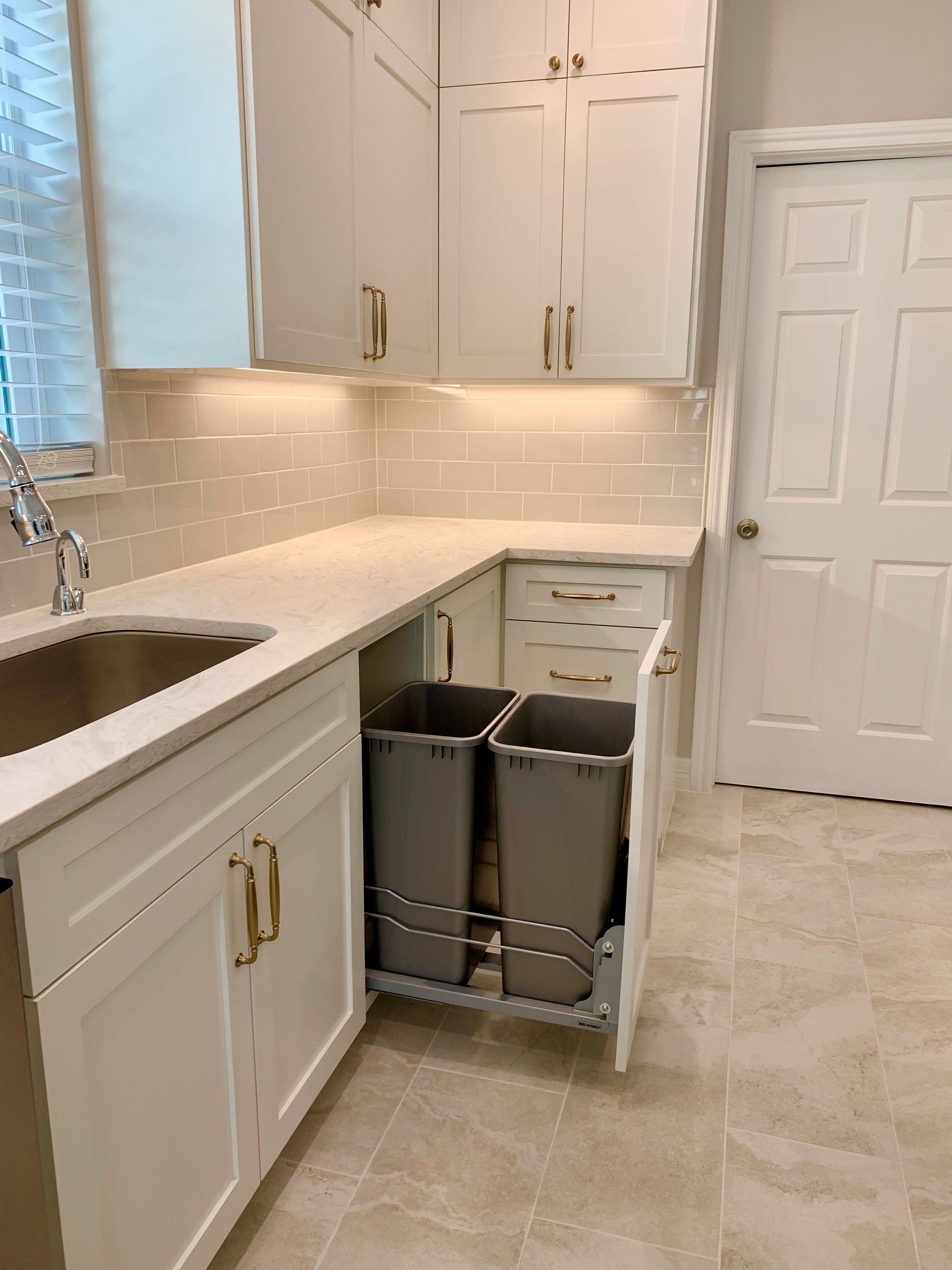 Bright white kitchen with granite counters, sink, cabinets, and a pull-out trash bin near the door