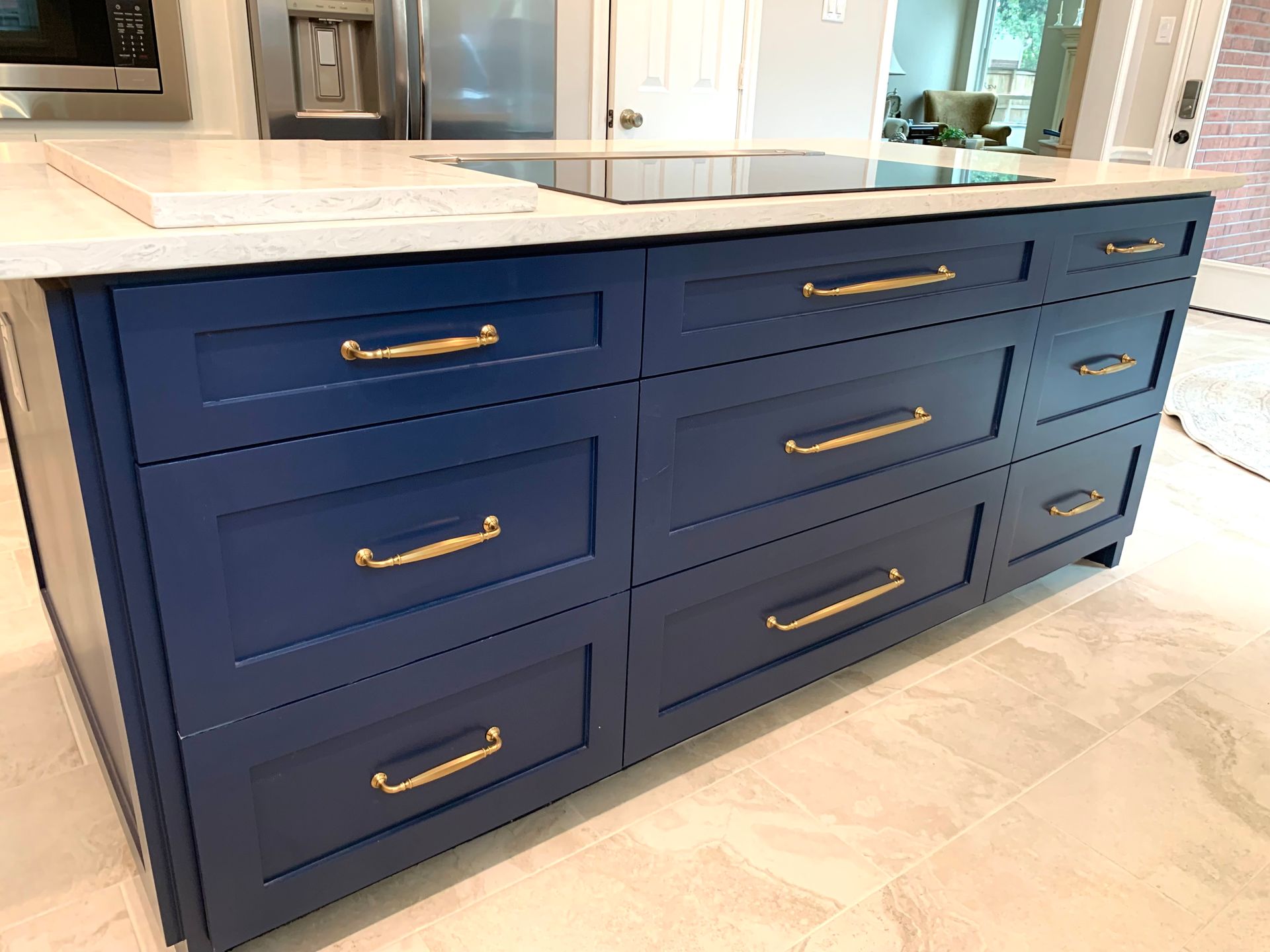 Dark navy kitchen island with brass handles and a light stone countertop in a bright kitchen