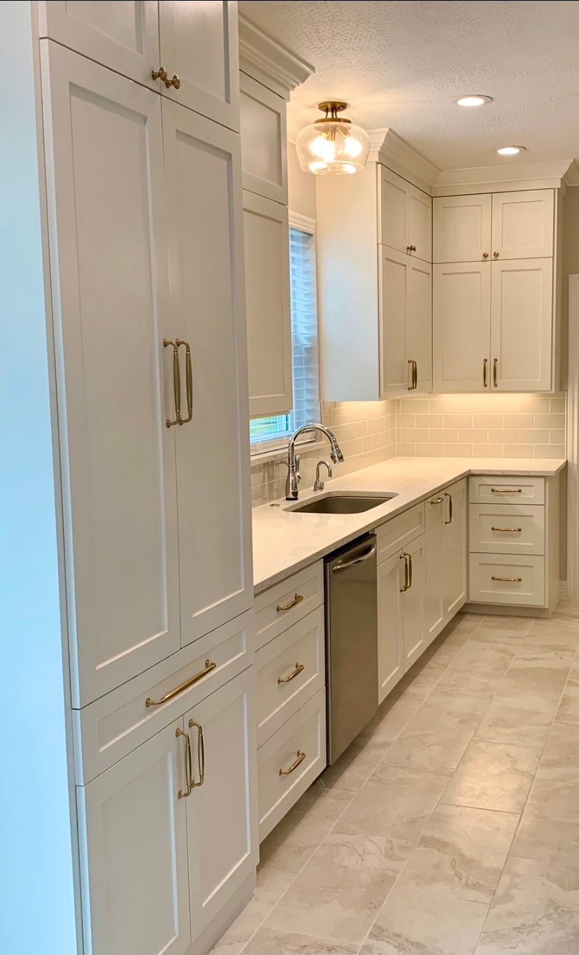 Bright white galley kitchen with tall cabinets, marble countertops, and recessed lighting.