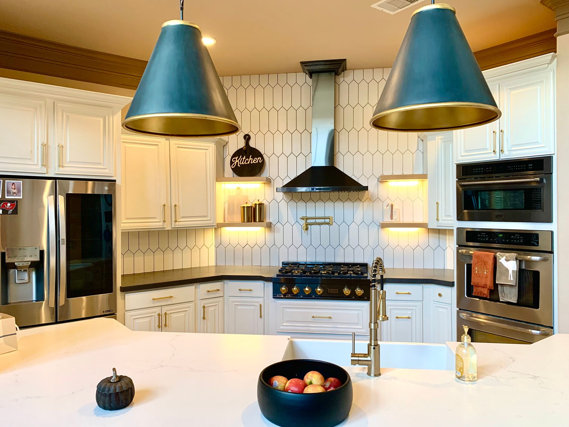Modern kitchen with white cabinets, stainless appliances, blue pendant lights, and a large white island with fruit bowl.