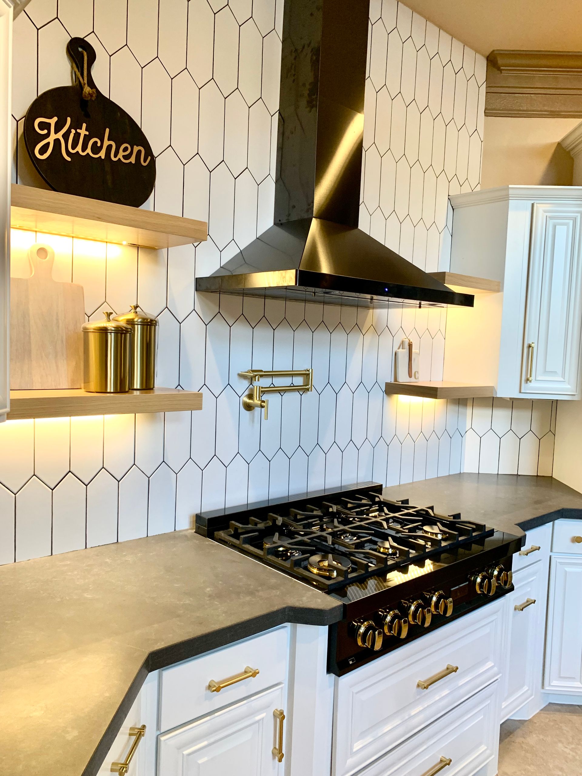 Modern white kitchen with black range hood, gold accents, and patterned backsplash