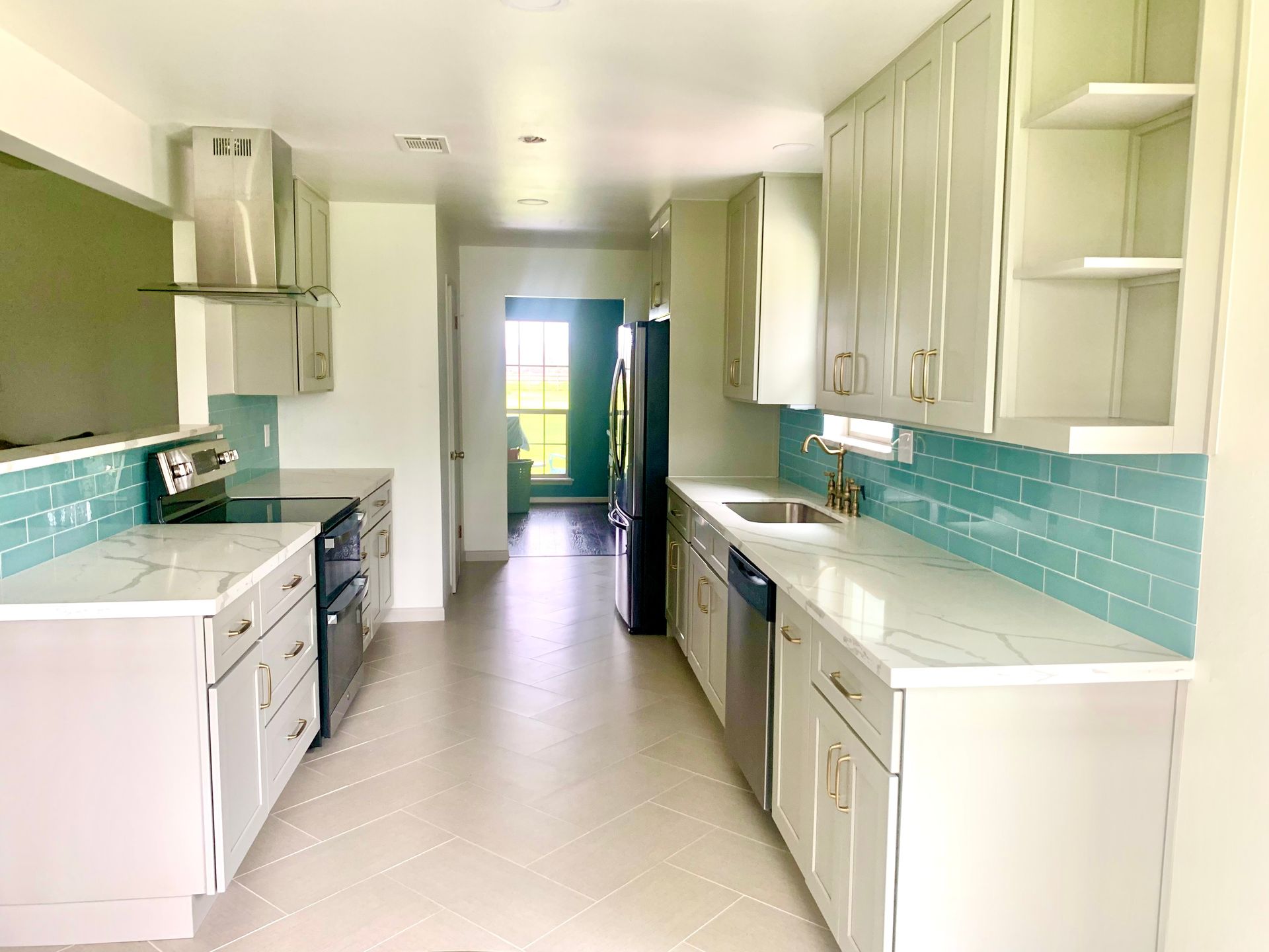 Bright galley kitchen with white cabinets, turquoise backsplash, and a view to the outside door.