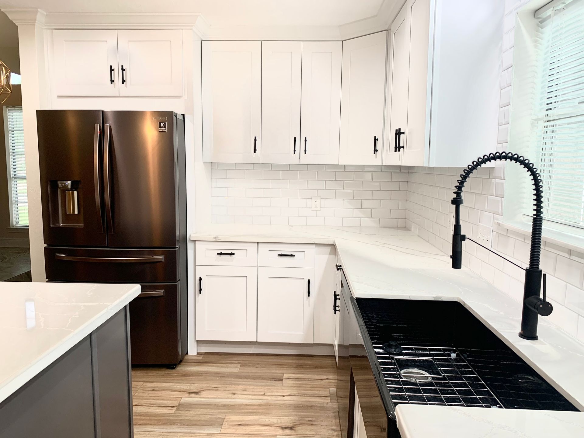 Bright modern kitchen with black appliances, white cabinets, wood floor, and black faucet.