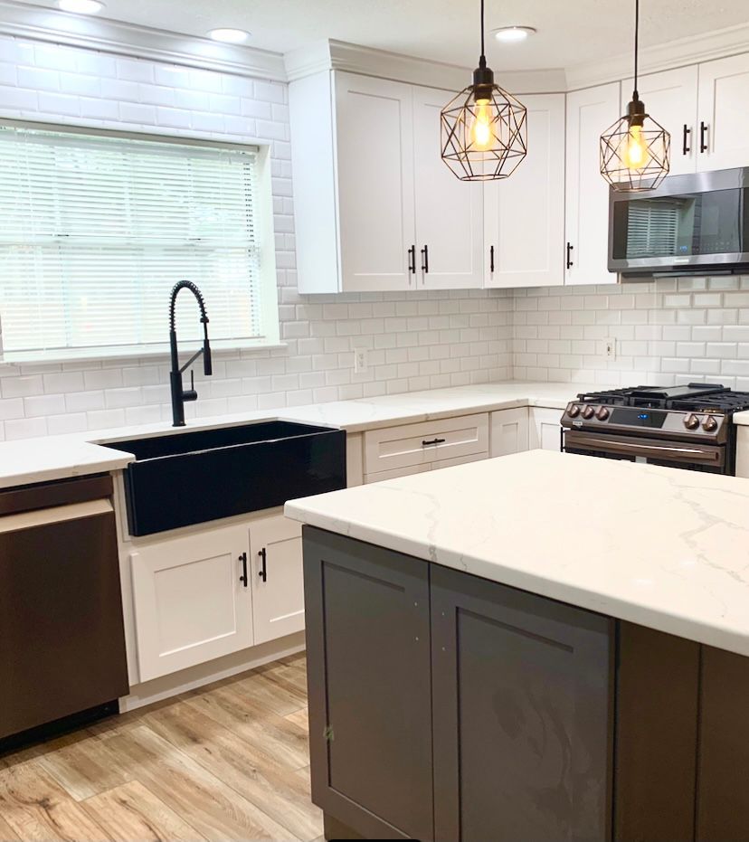 Bright modern kitchen with white cabinets, dark island, farmhouse sink, and pendant lights