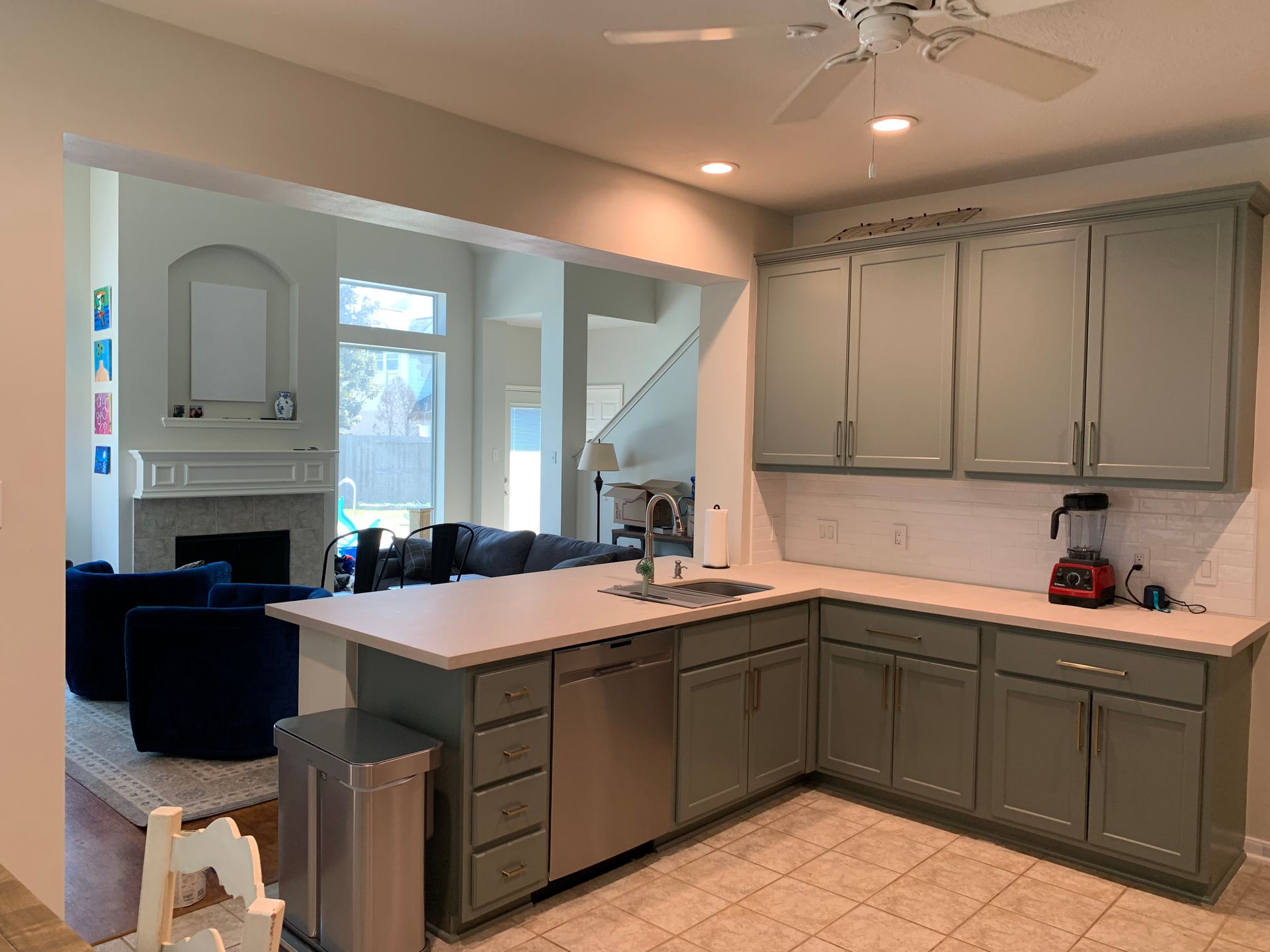 Open kitchen with gray cabinets, white countertops, and a view into a living room with a fireplace.