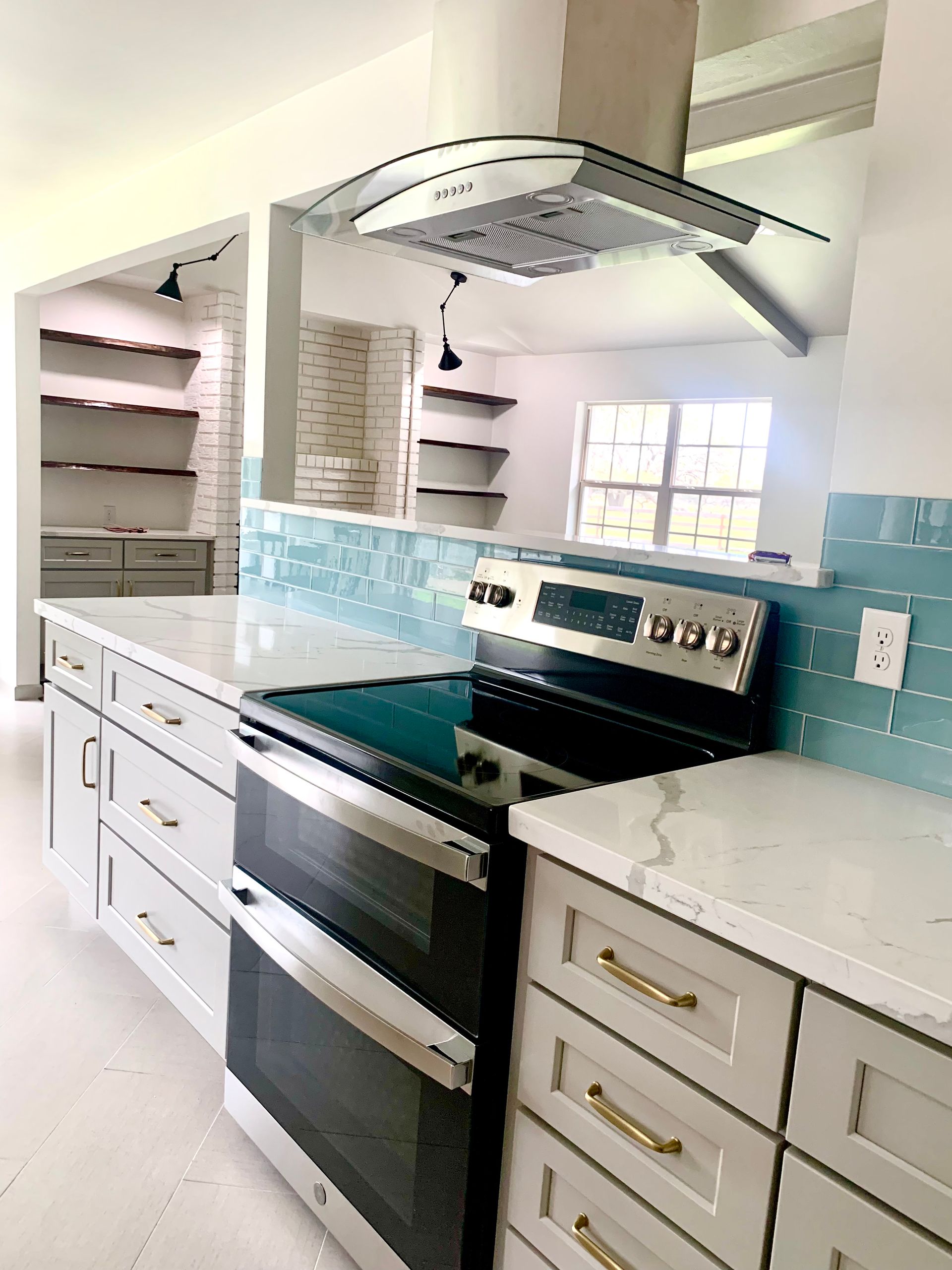 Bright kitchen with black stove, white cabinets, turquoise backsplash, and stainless range hood.