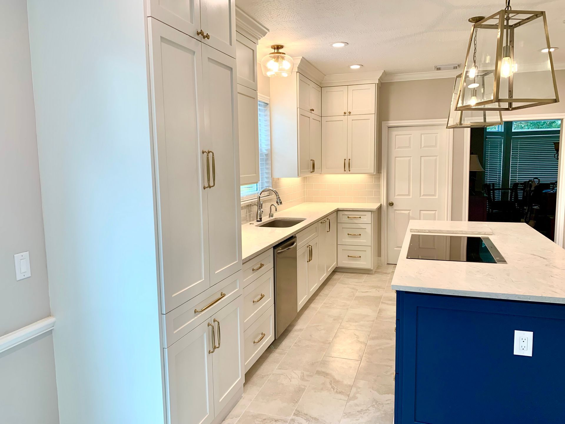 Modern white kitchen with blue island, pendant lights, and built-in cabinets