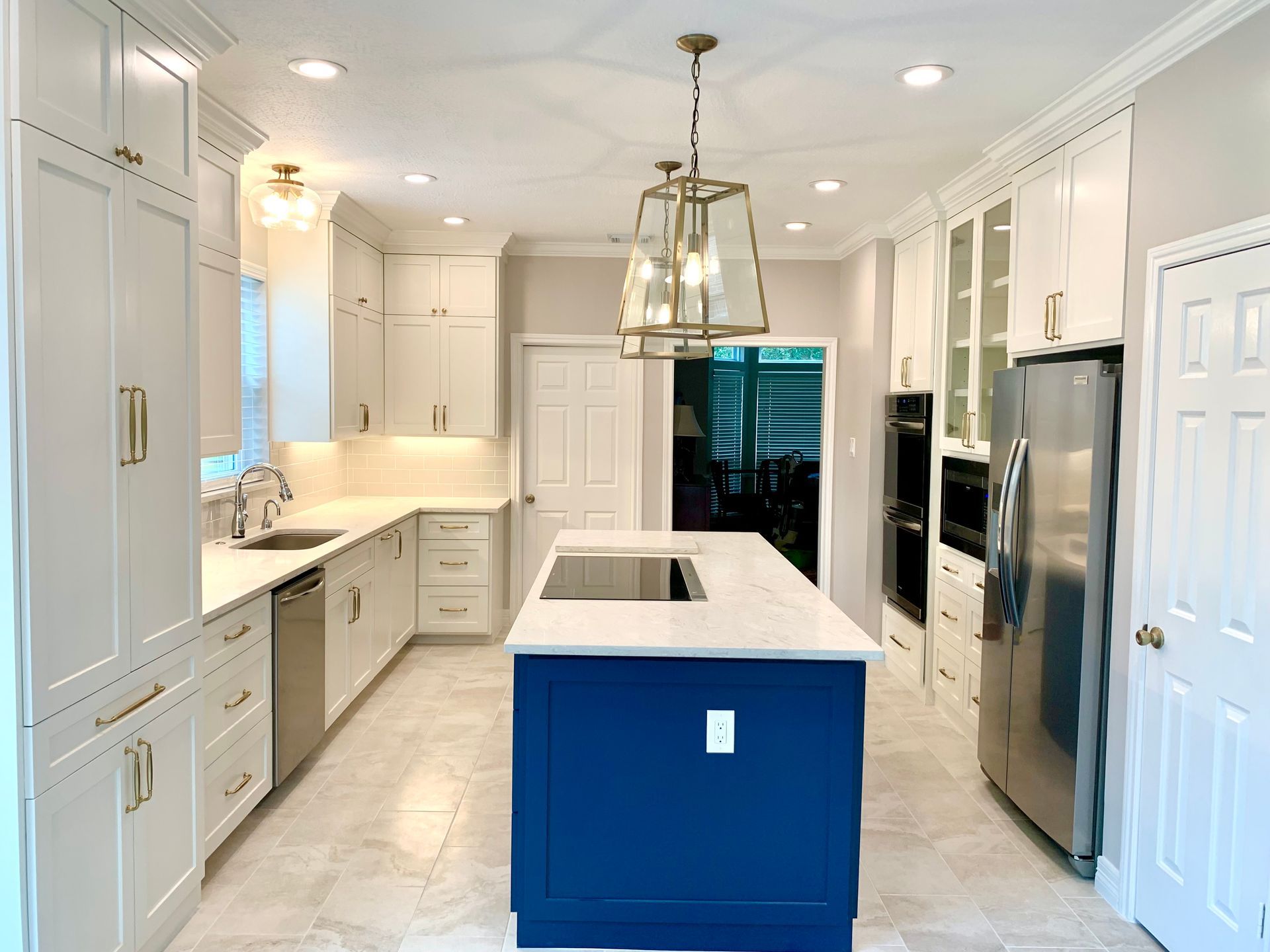Bright white kitchen with blue island, marble countertops, and glass pendant lights