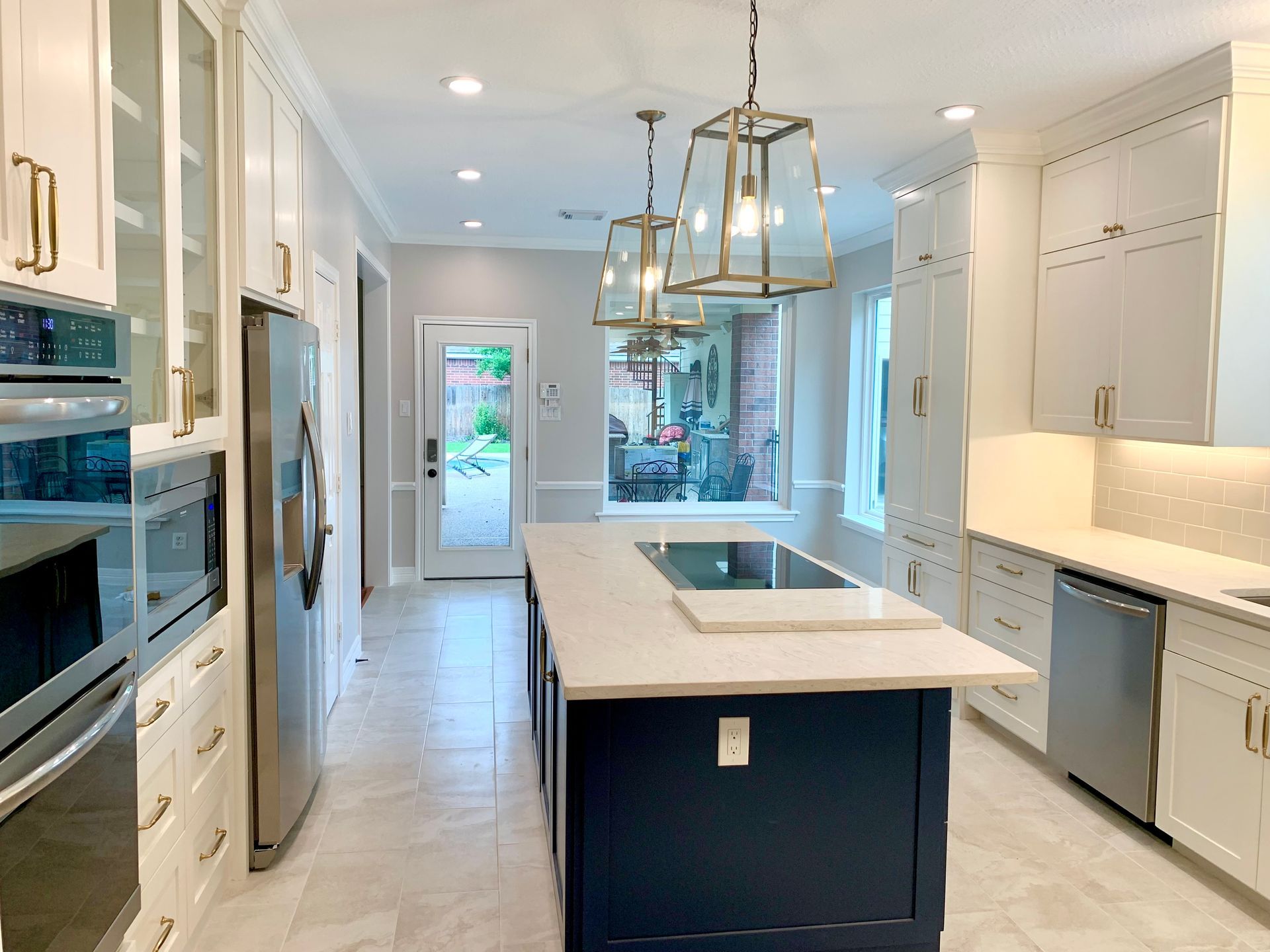 Bright modern kitchen with white cabinetry, marble island, and brass pendant lights
