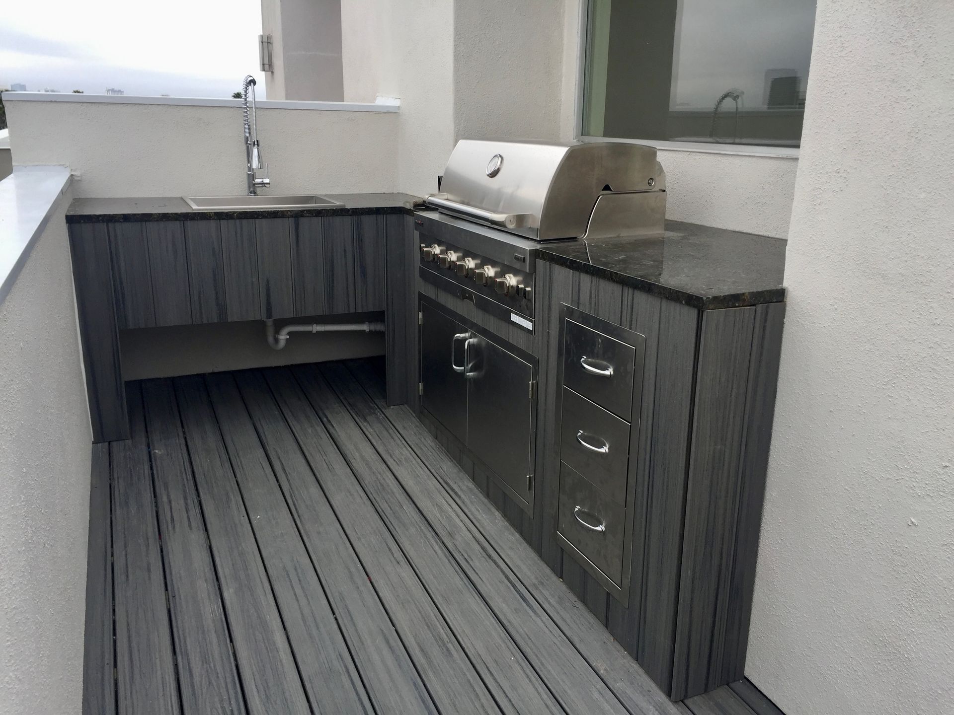 Outdoor patio with gray cabinets, stainless grill, and sink on a wood-look deck.