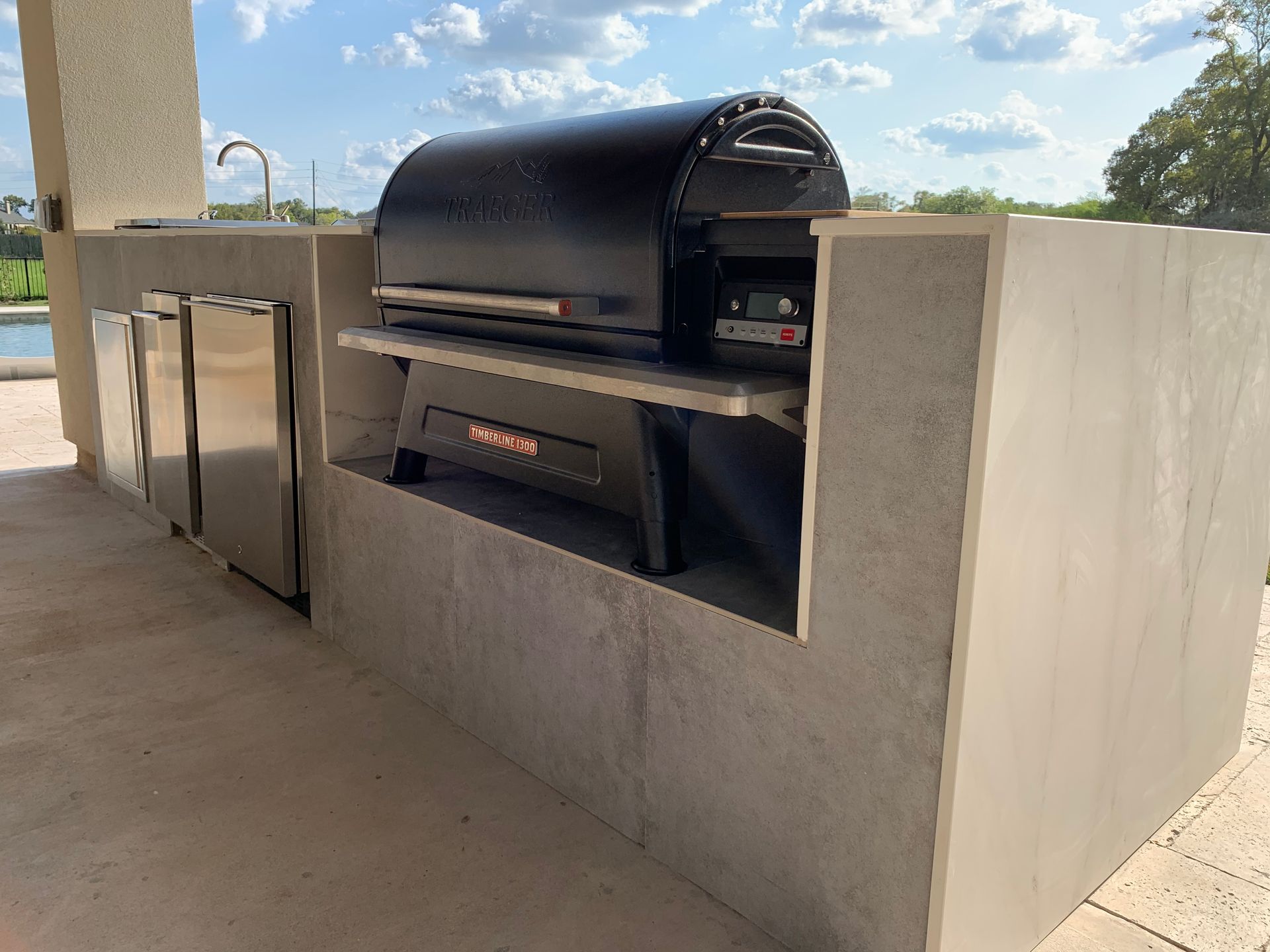Outdoor built-in black barbecue grill on a concrete patio under a covered structure.