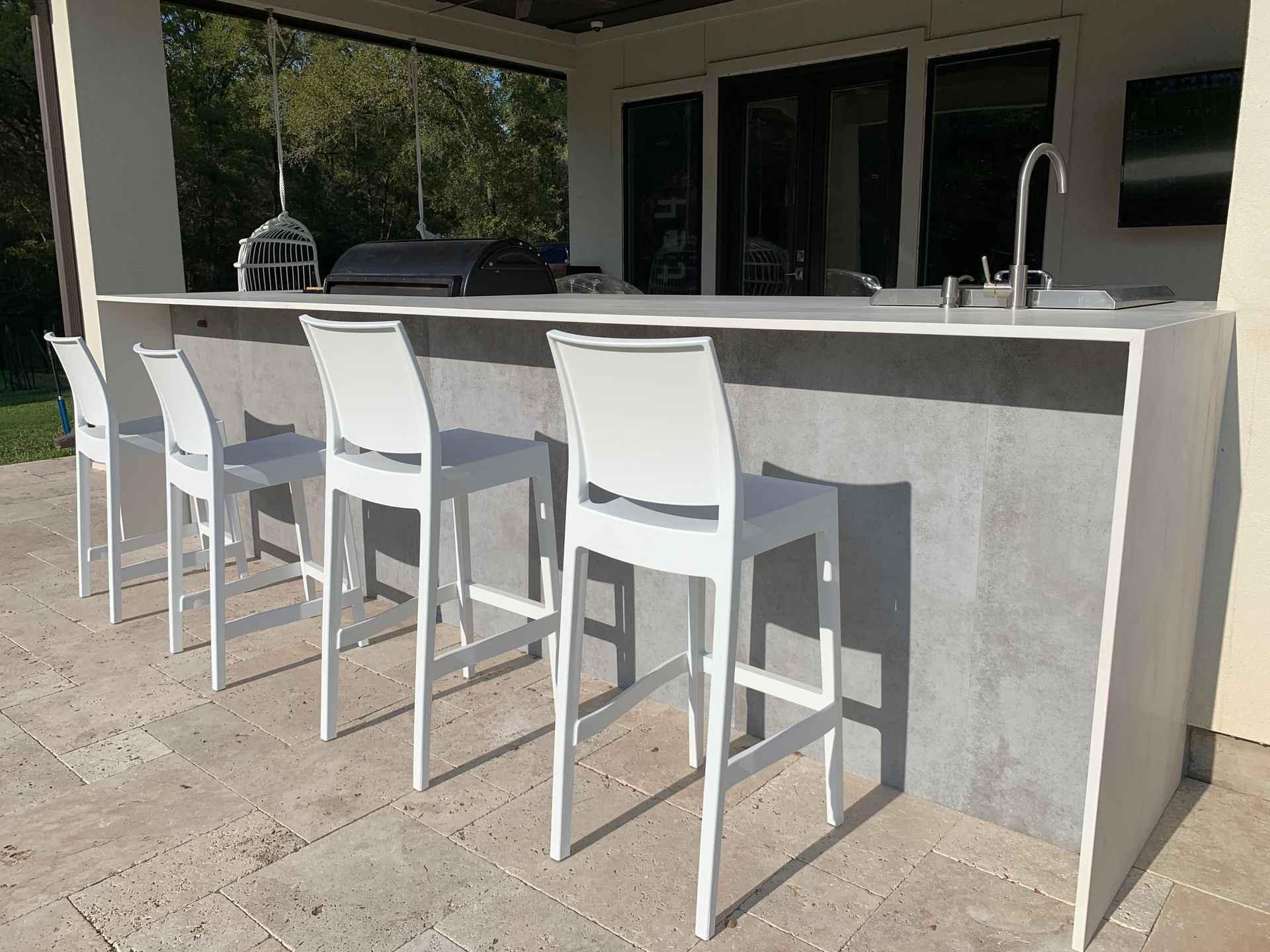 White bar stools lined up at an outdoor concrete patio counter beside a house.