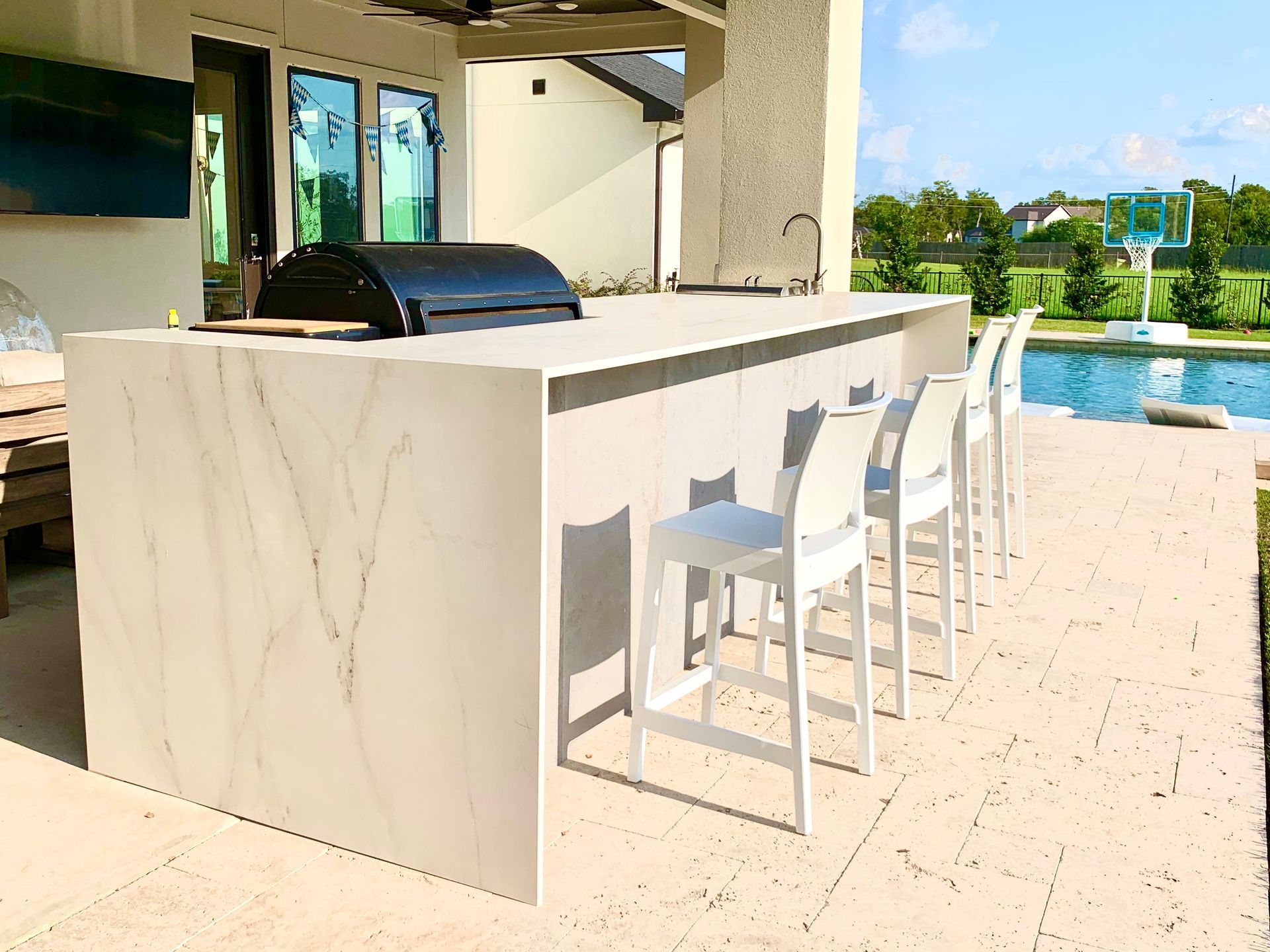 Outdoor poolside bar with white stools and a marble counter beside a bright blue pool