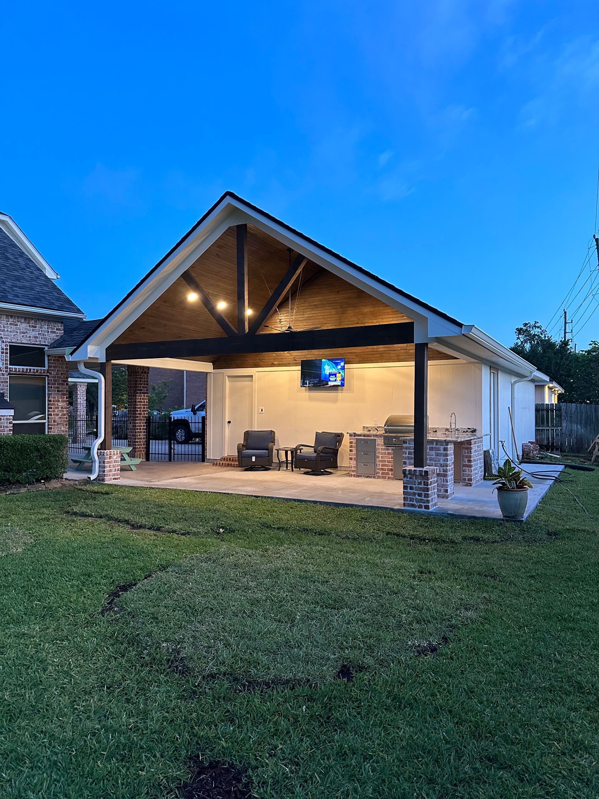 Covered backyard patio at dusk with outdoor seating, warm lights, and a grassy lawn