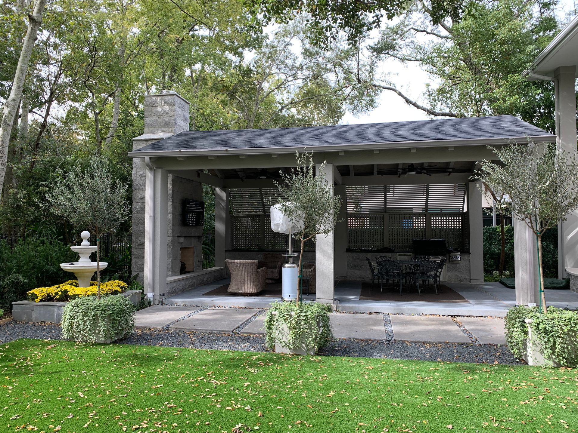 Covered patio with stone fireplace, seating, and fountain in a landscaped backyard