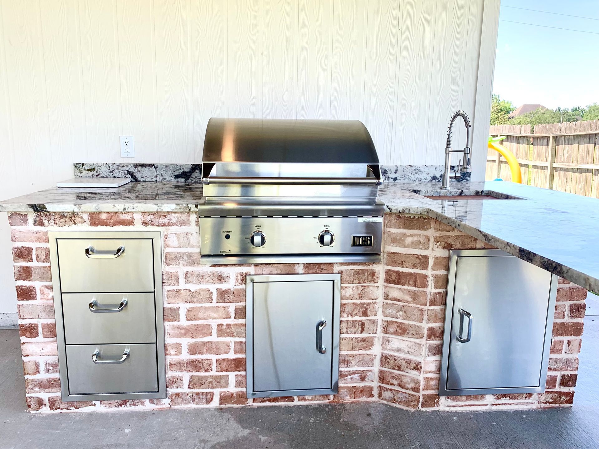 Built-in outdoor brick grill with stainless steel cabinets and countertop on a patio
