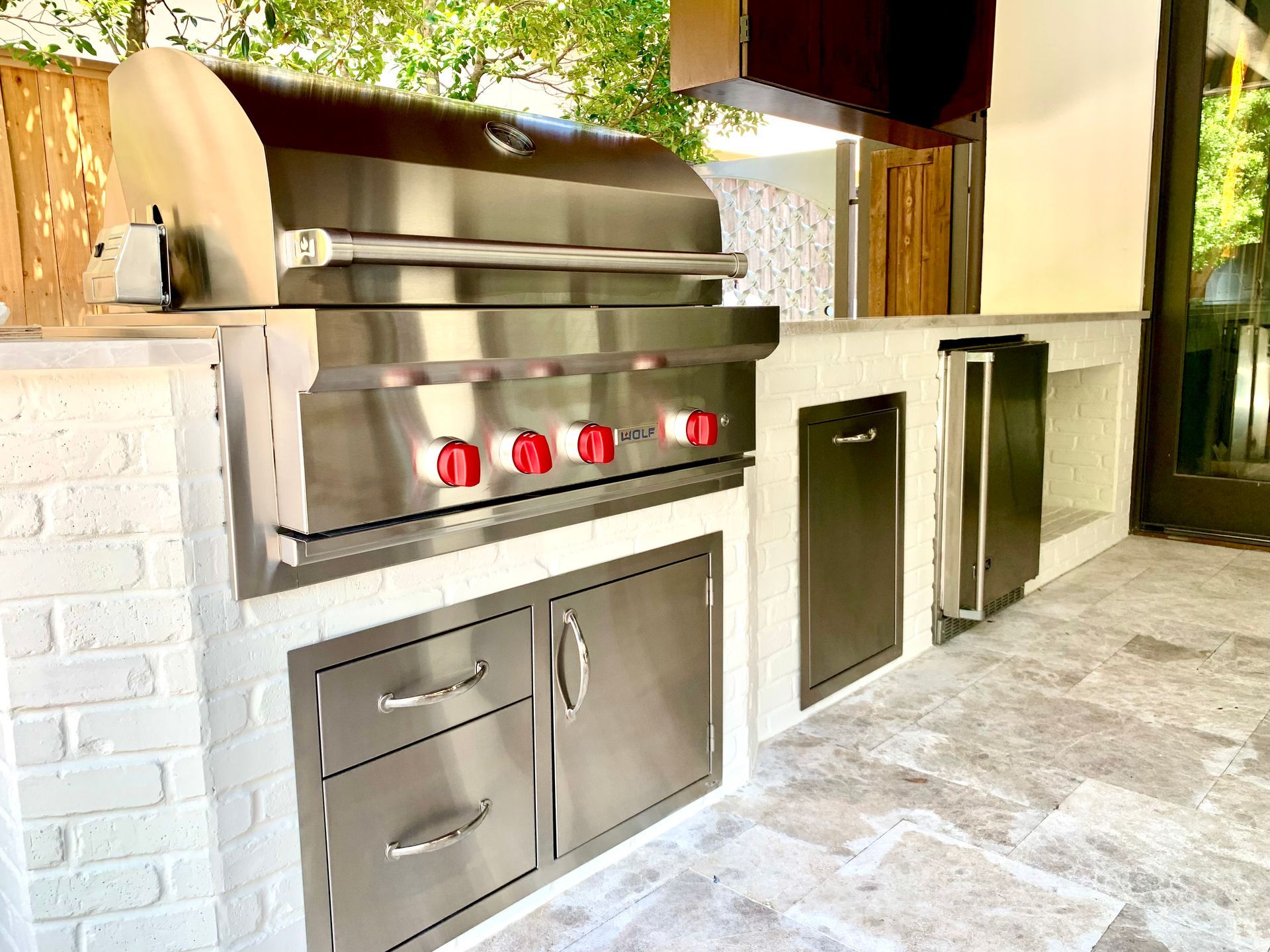 Outdoor stainless-steel grill station with red knobs beside a brick wall and stone patio