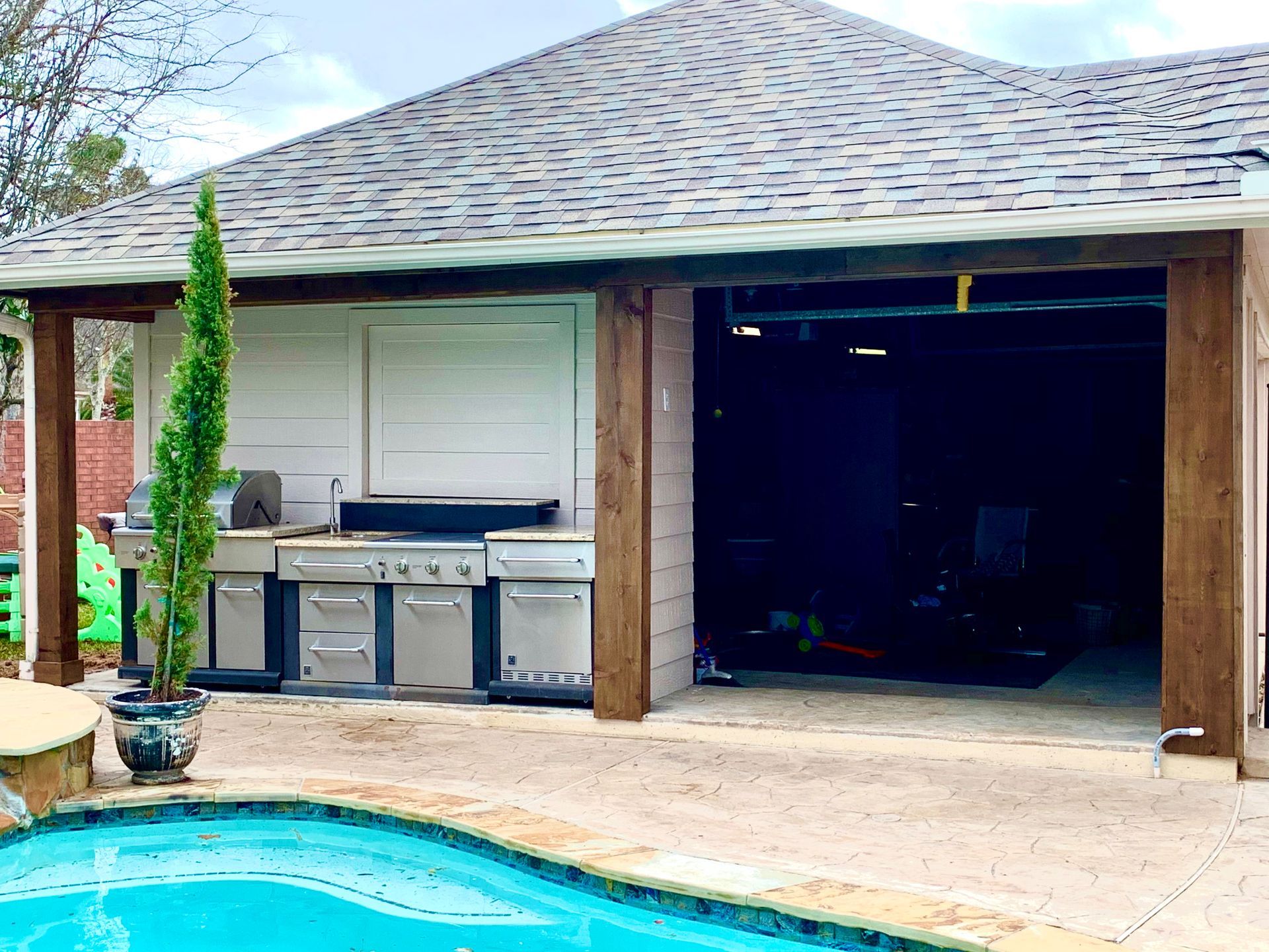 Backyard pool beside a covered patio with outdoor kitchen and open garage door
