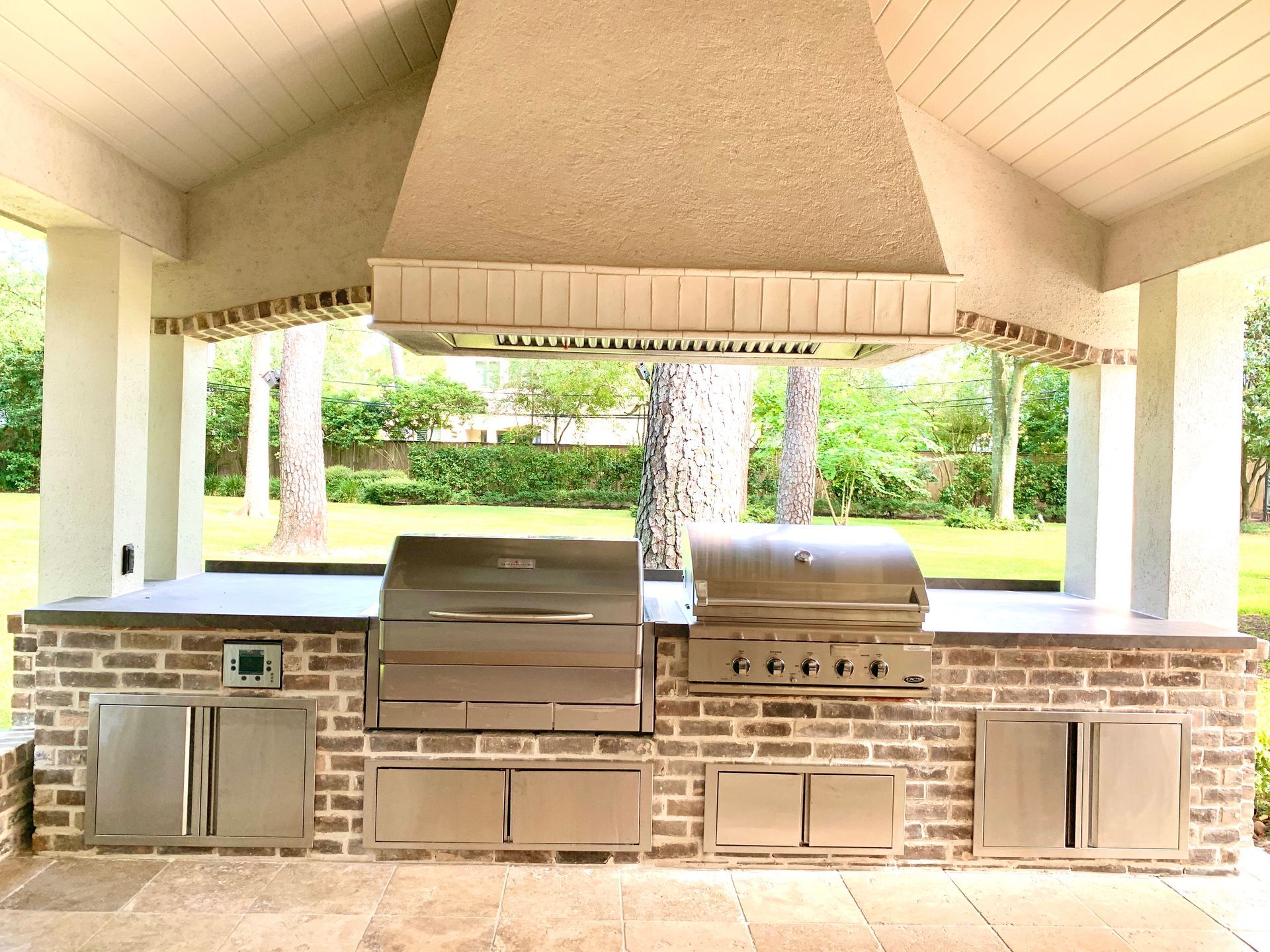 Covered outdoor kitchen with built-in grill, sink, and brick countertops under a pavilion