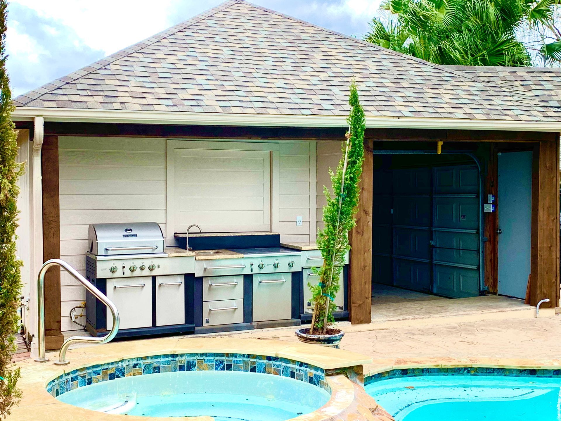 Backyard patio with grill, blue hot tub, and small pool beside a house and garage