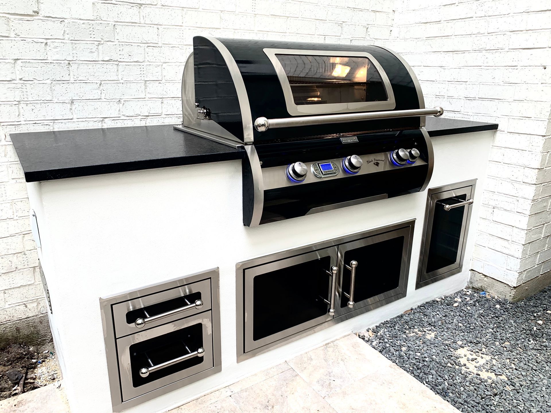Outdoor built-in gas grill with black and stainless steel finish against a white brick wall