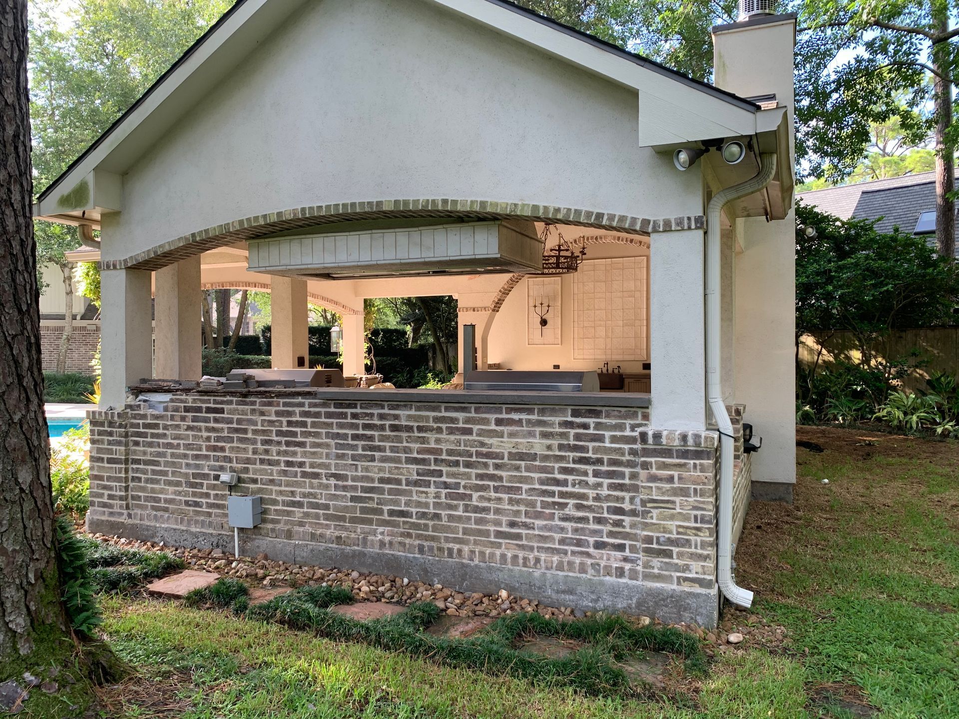Outdoor pavilion with stone half-wall, open arches, and a white roof in a grassy yard.