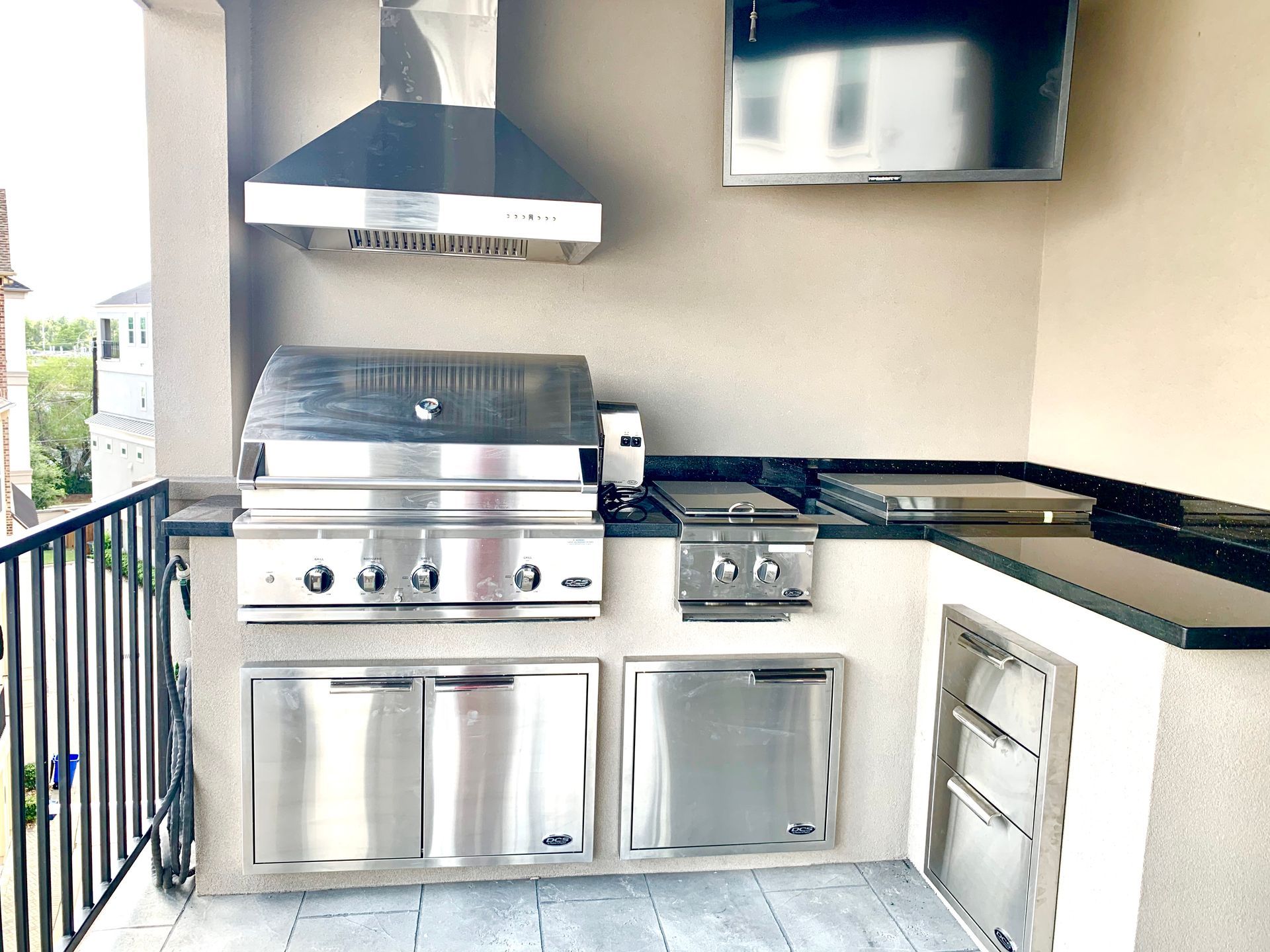 Outdoor patio kitchen with stainless steel grill, sink, cabinets, and wall-mounted TV