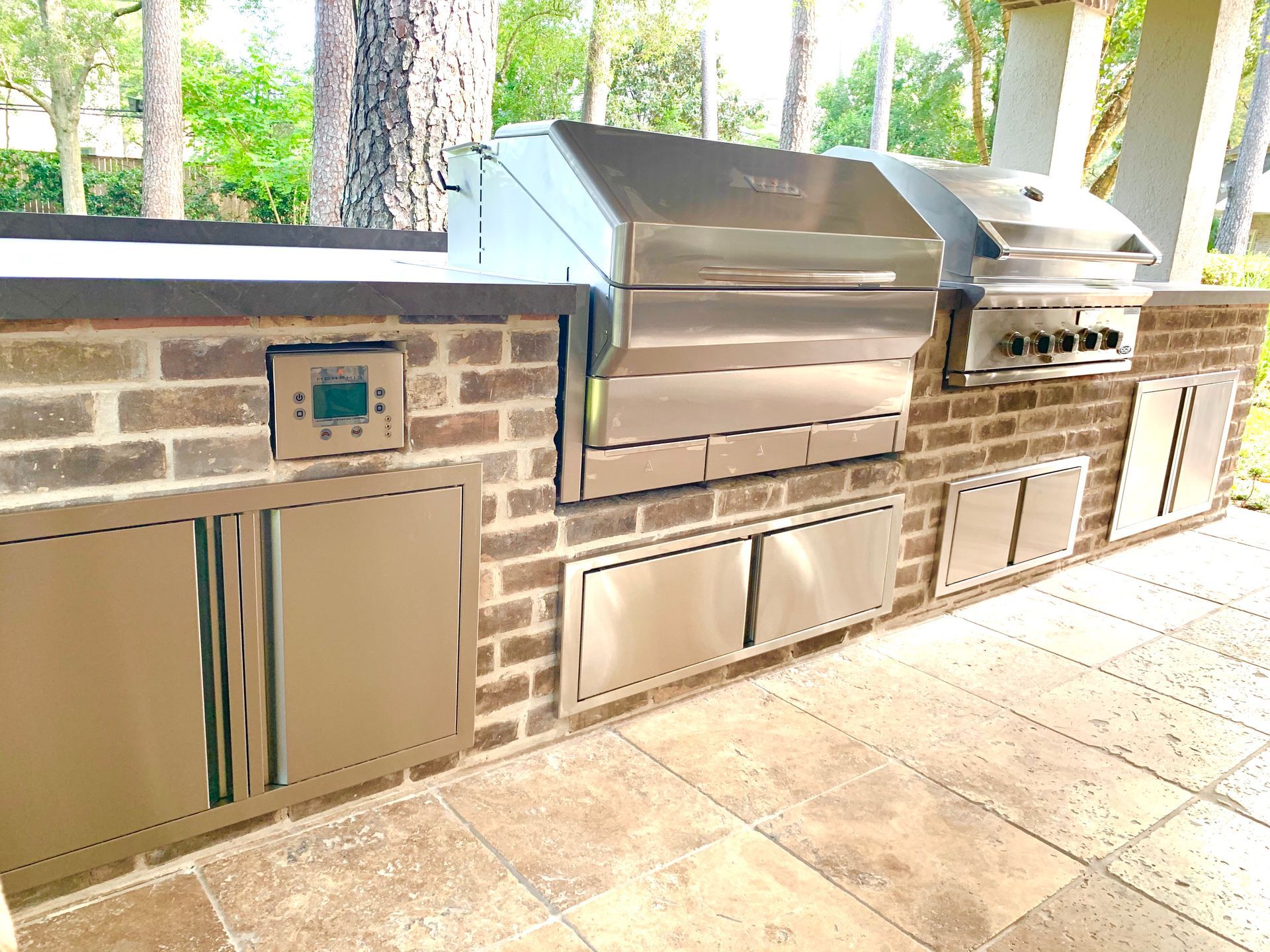 Outdoor brick kitchen with stainless steel grill, cabinets, and sink under a covered patio